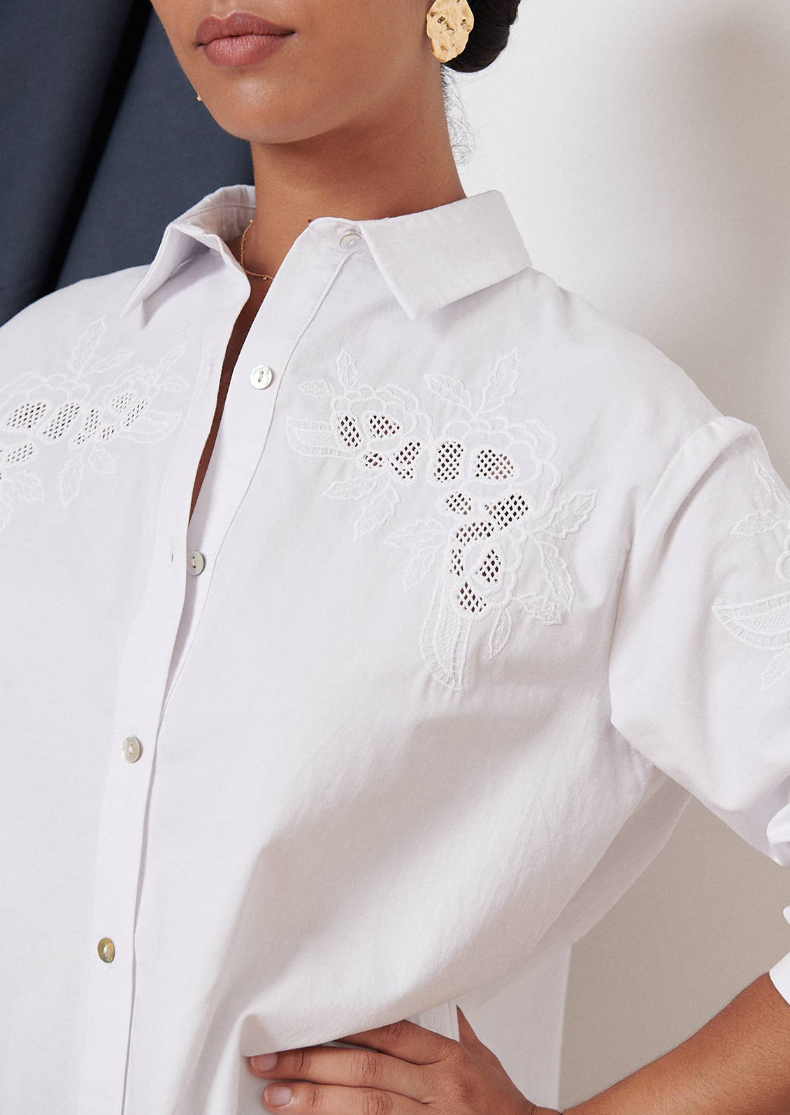 A woman wearing a white button down shirt with eyelet embroidery at yoke.