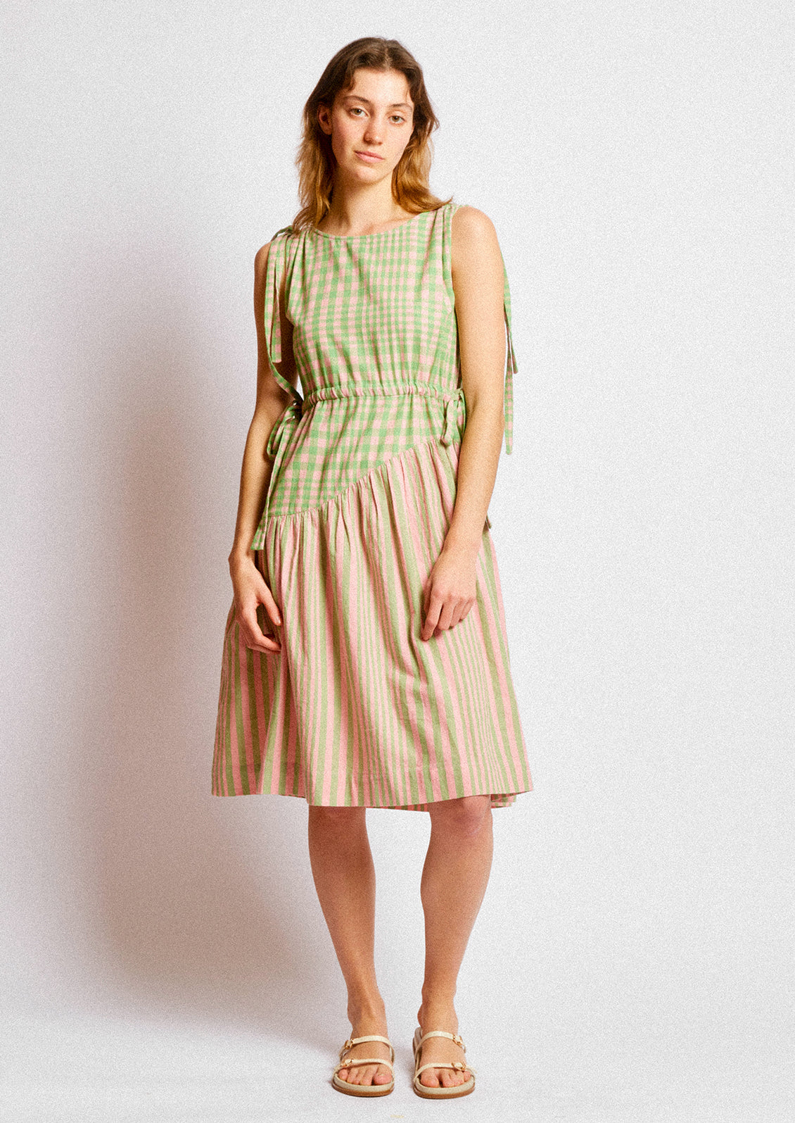 A person wearing a short dress in green and pink striped mix stripe and gingham.