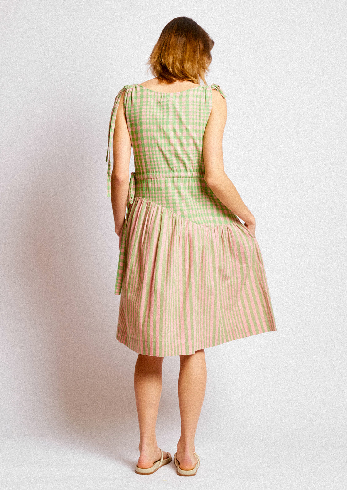 A person wearing a short dress in green and pink striped mix stripe and gingham.