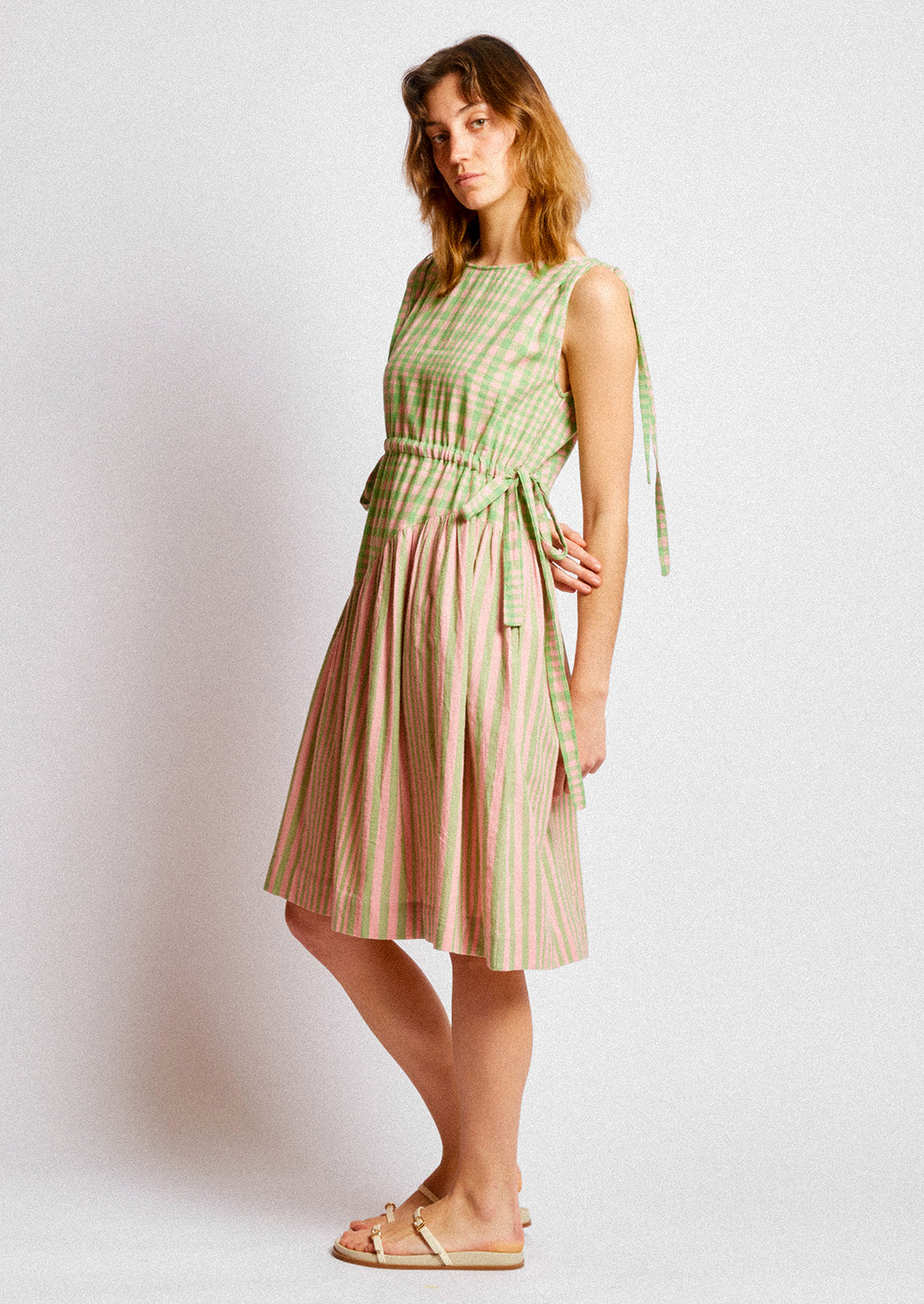 A person wearing a short dress in green and pink striped mix stripe and gingham.