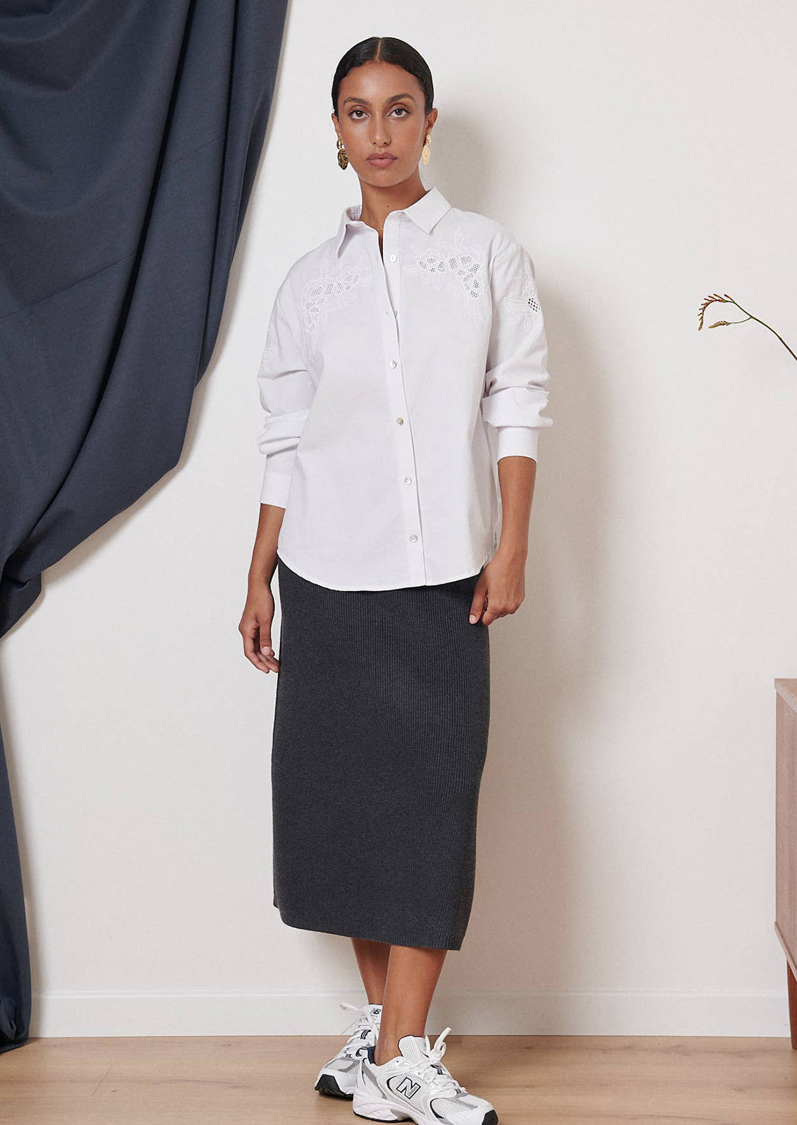 A woman wearing a white button down shirt with eyelet embroidery at yoke.