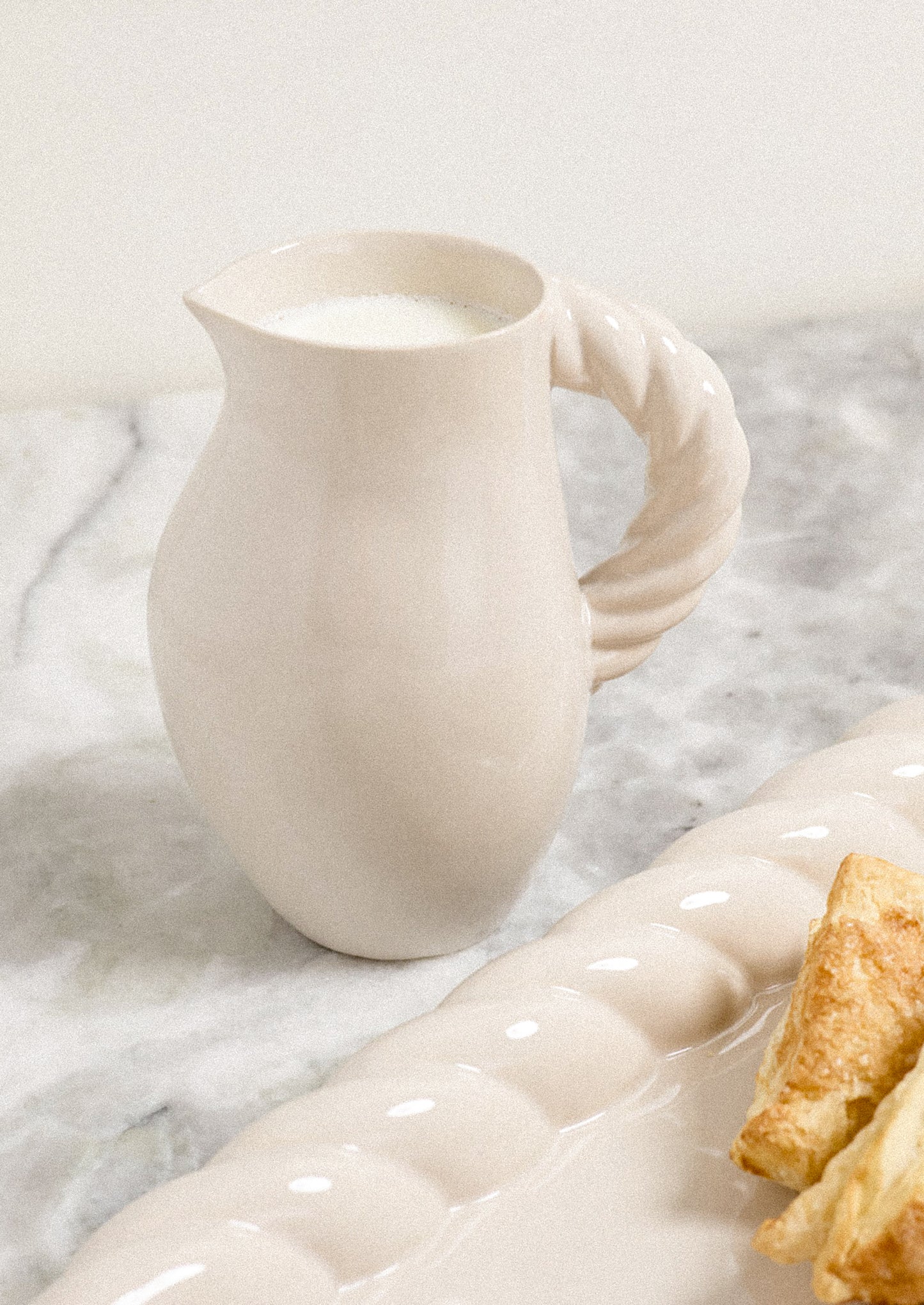 A white ceramic pitcher with braided textured handle.