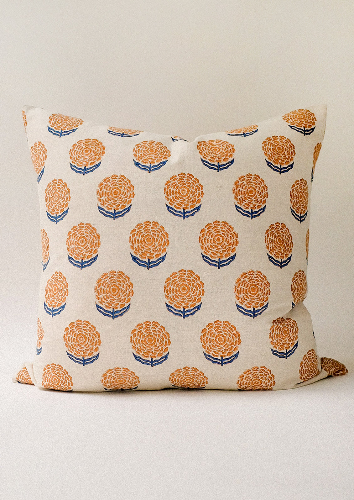 A block printed pillow with orange and blue marigold pattern.