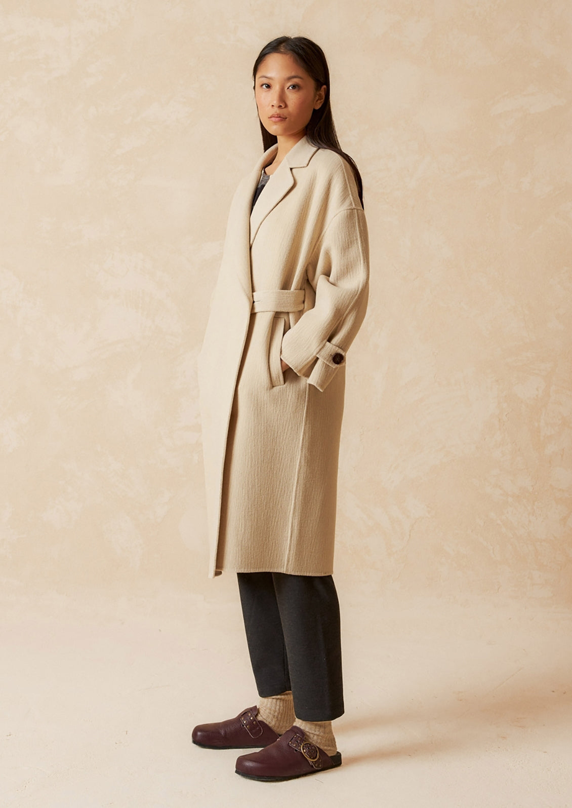 A woman wearing a wool coat with subtle texture and tab closure.