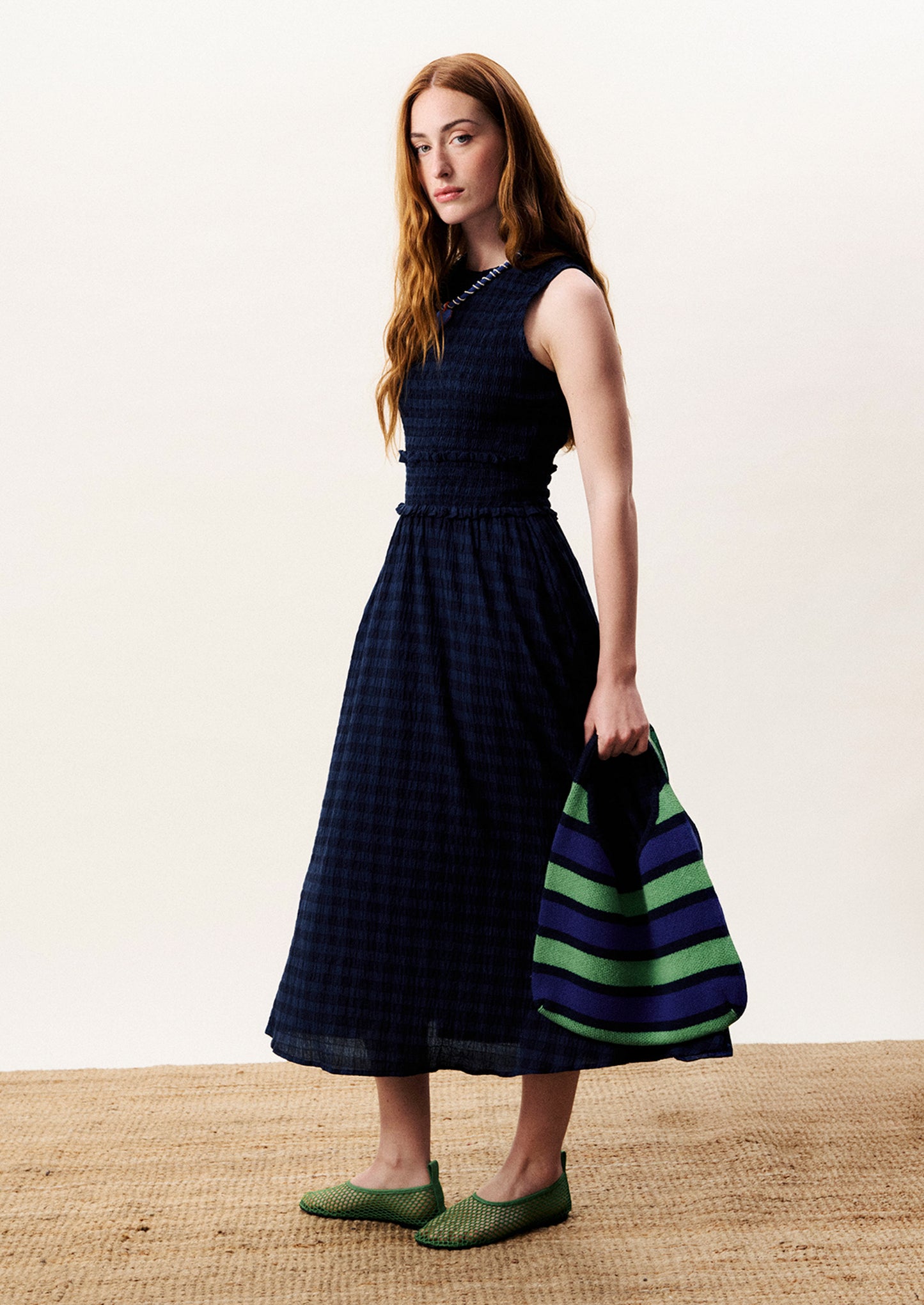 Woman wearing a dark blue dress with a striped bag on a neutral background