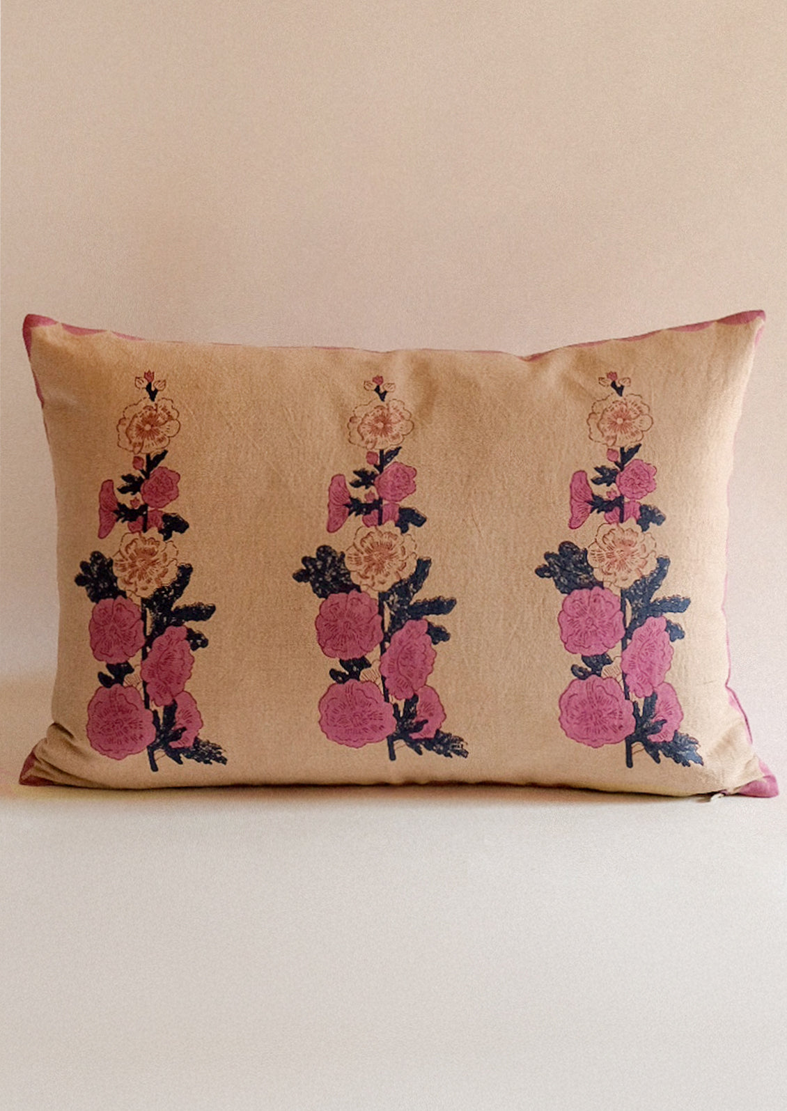 A beige throw pillow with pink block printed hollyhock pattern.