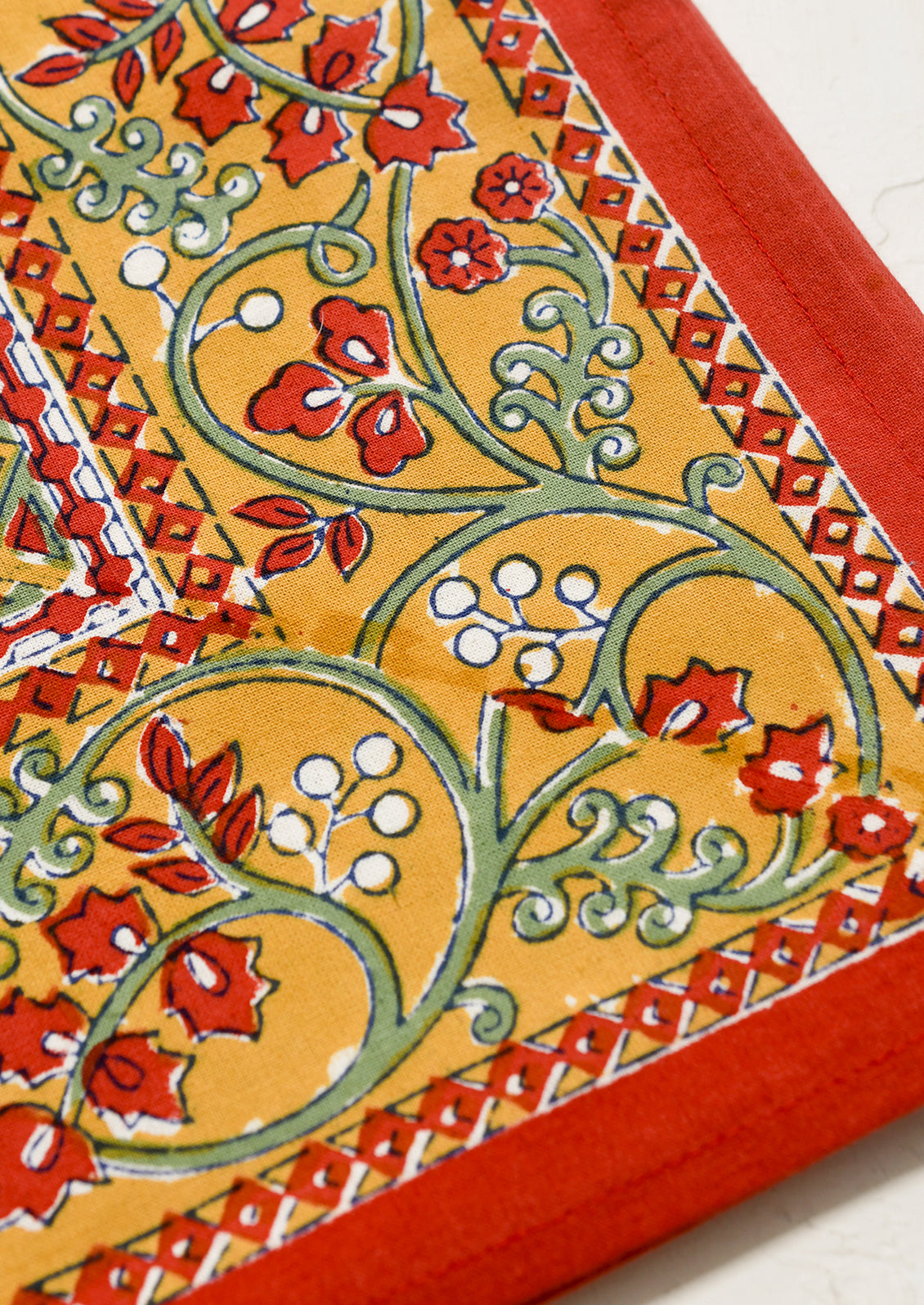A block printed tablecloth in red with mustard, blue and green floral print.