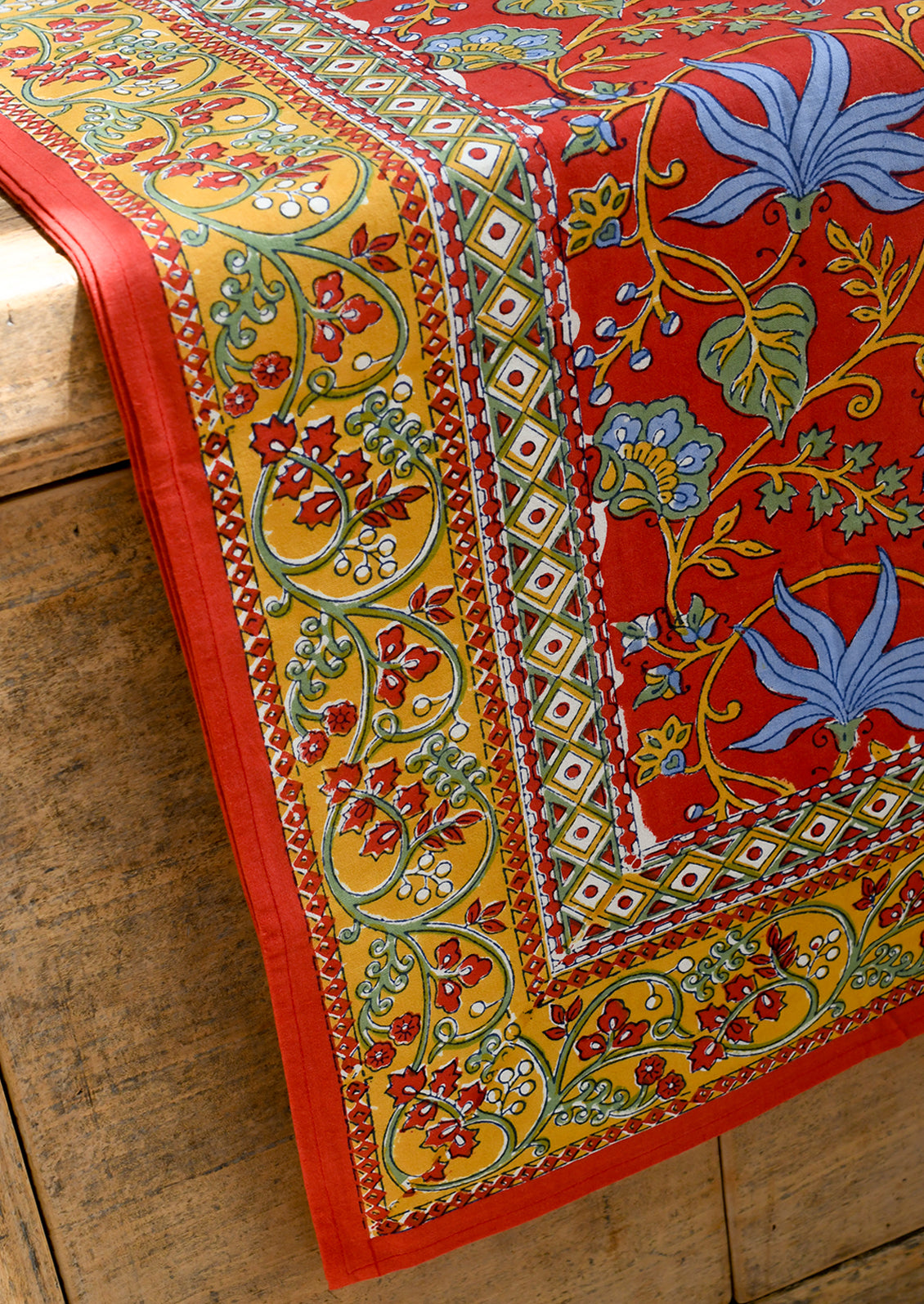 A block printed tablecloth in red with mustard, blue and green floral print.