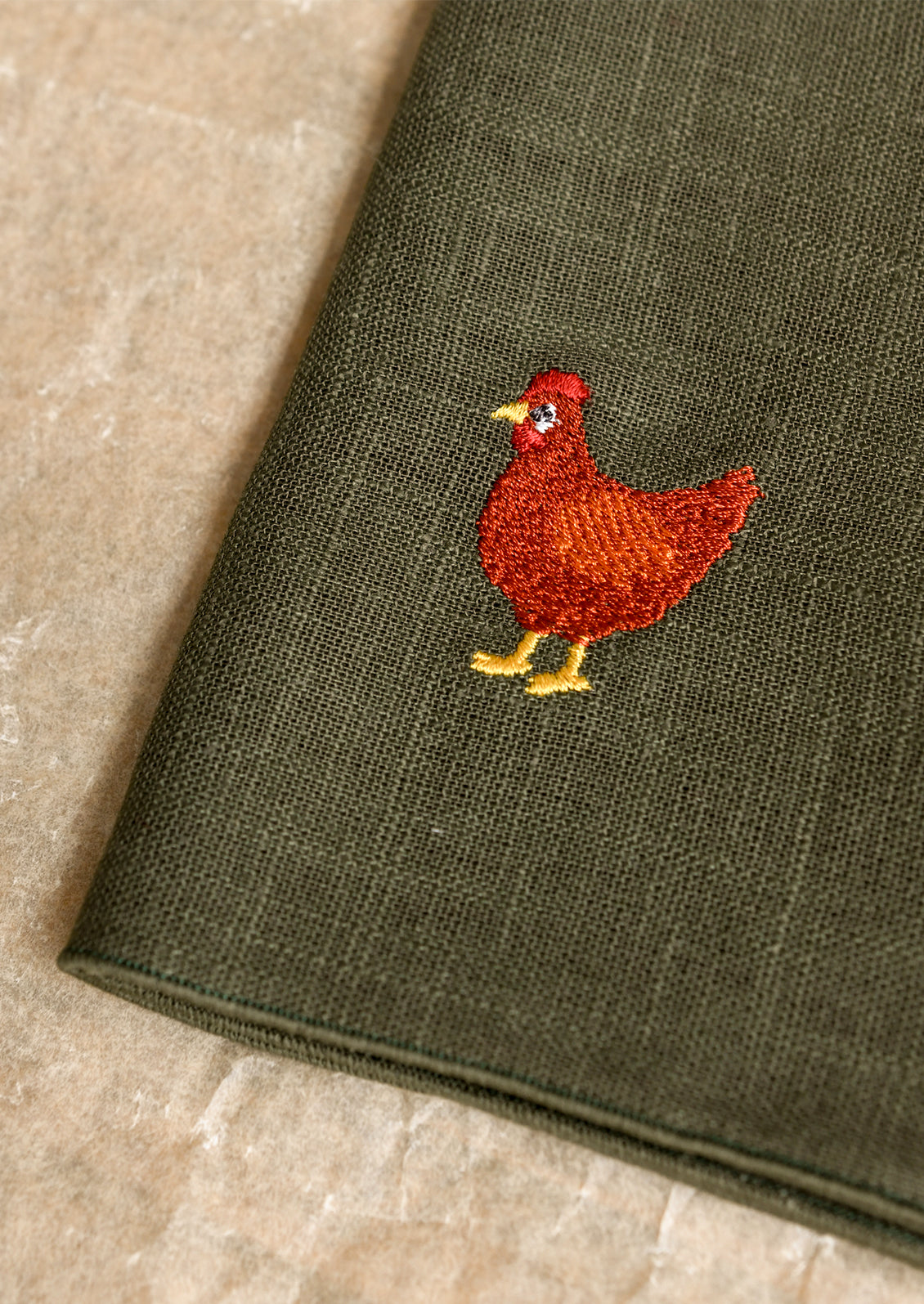 Green fabric with a red embroidered chicken design on a beige background
