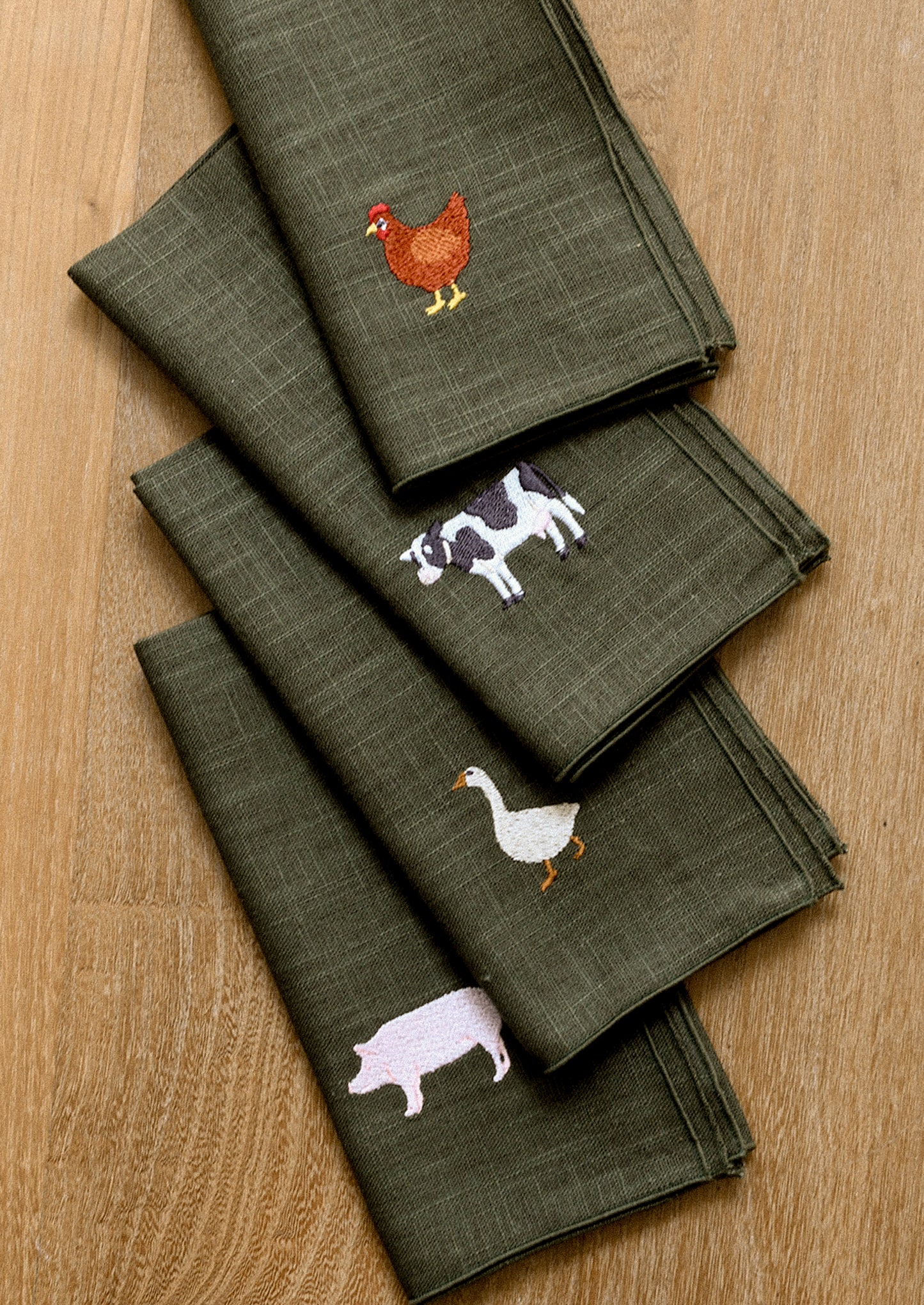 Set of green napkins with embroidered animal designs on a wooden surface