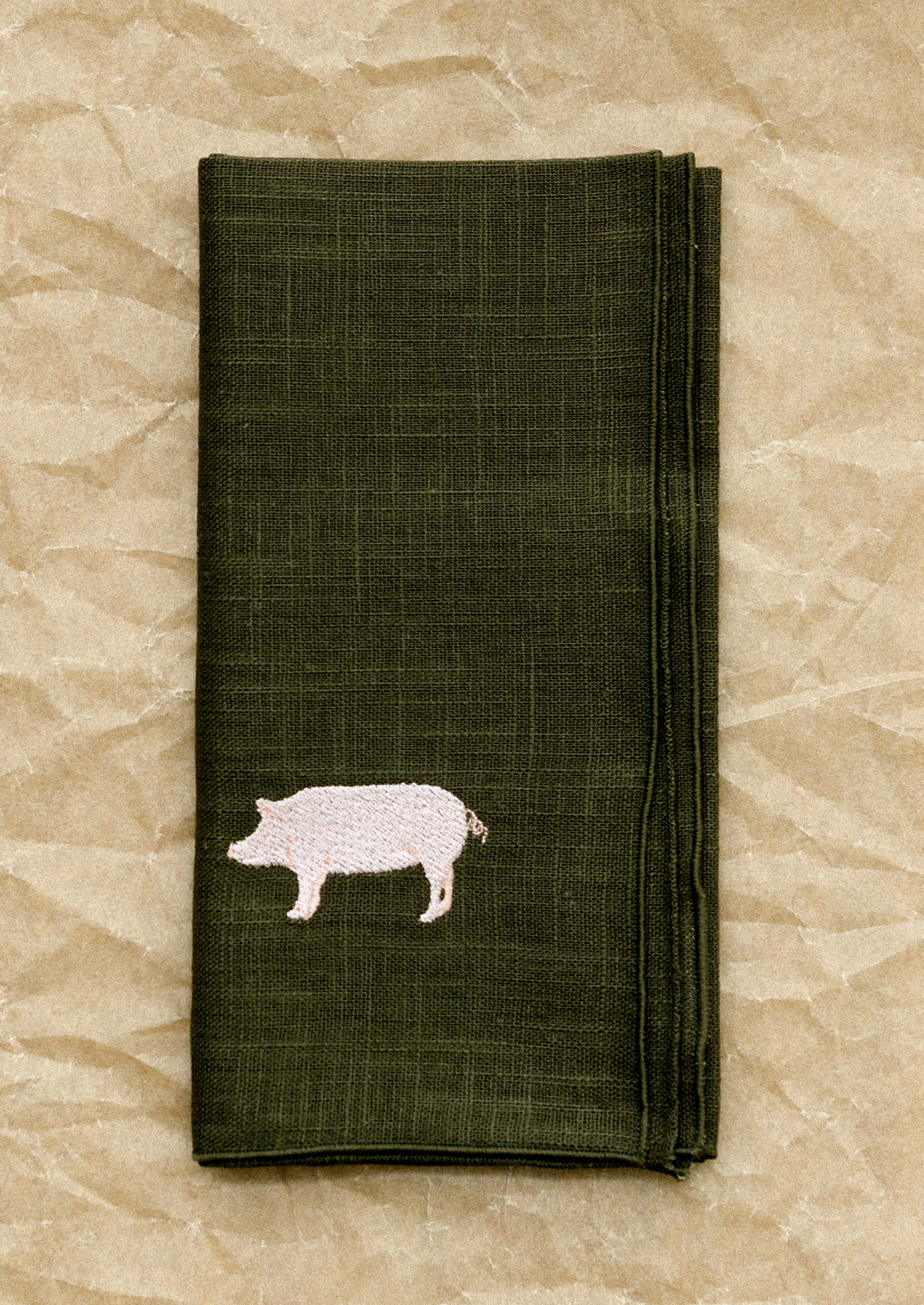 Folded dark green napkin with a pig design on a beige textured background