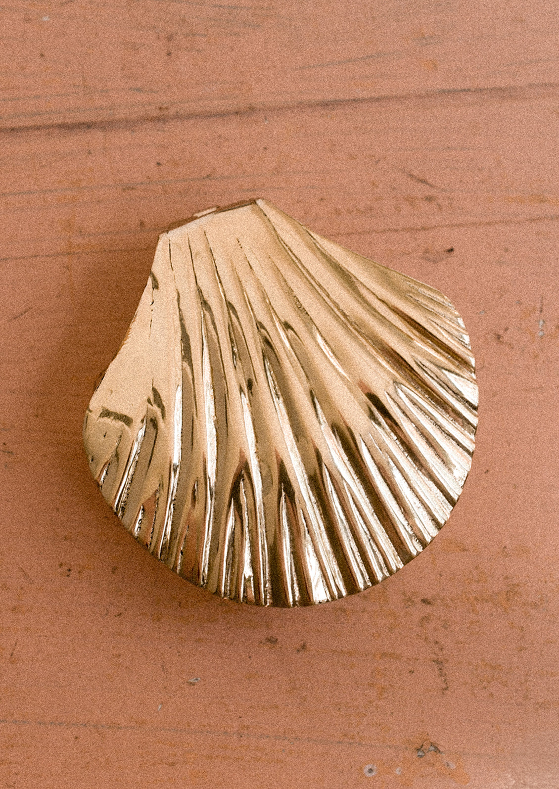 A gold shell-shaped trinket box on a wooden surface.