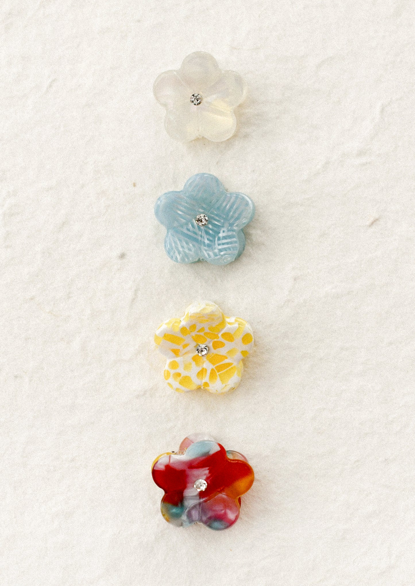 Set of four colorful flower-shaped hair claws on a textured white background