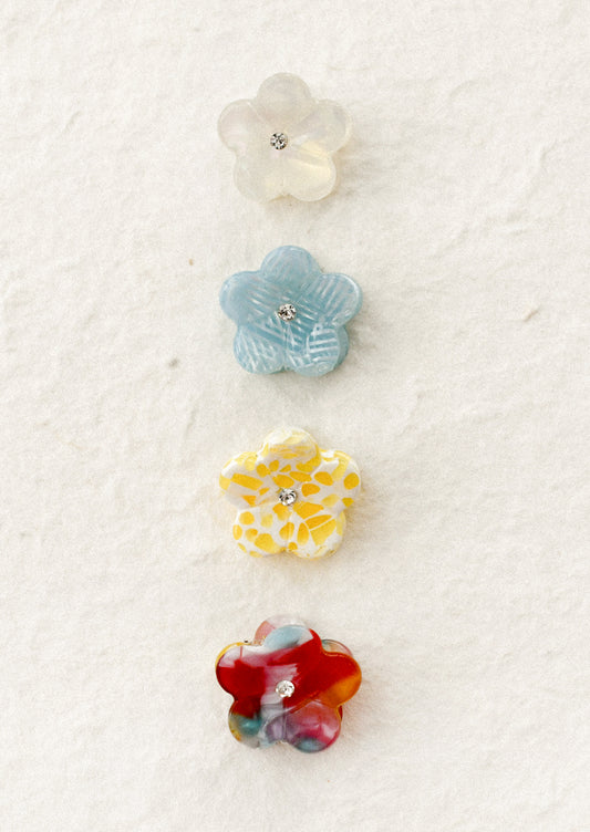 Set of four colorful flower-shaped hair claws on a textured white background