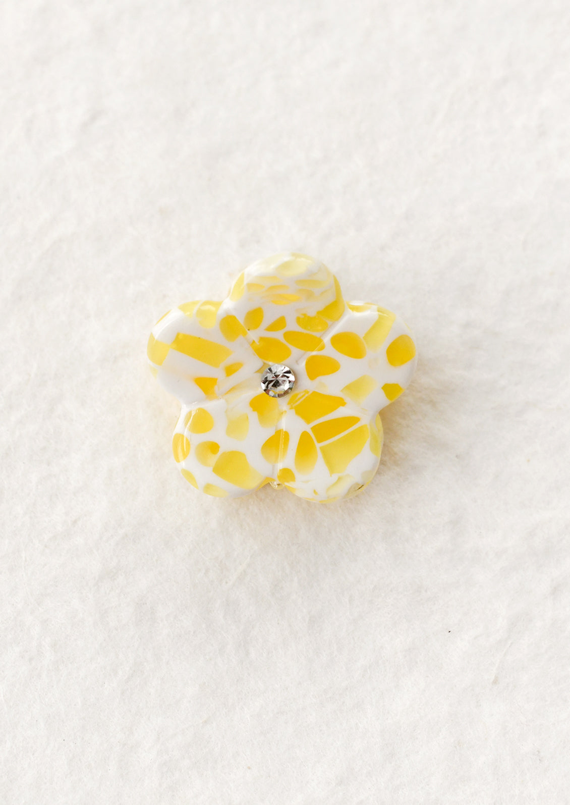 Yellow flower-shaped hair claw with a central gemstone on a white background