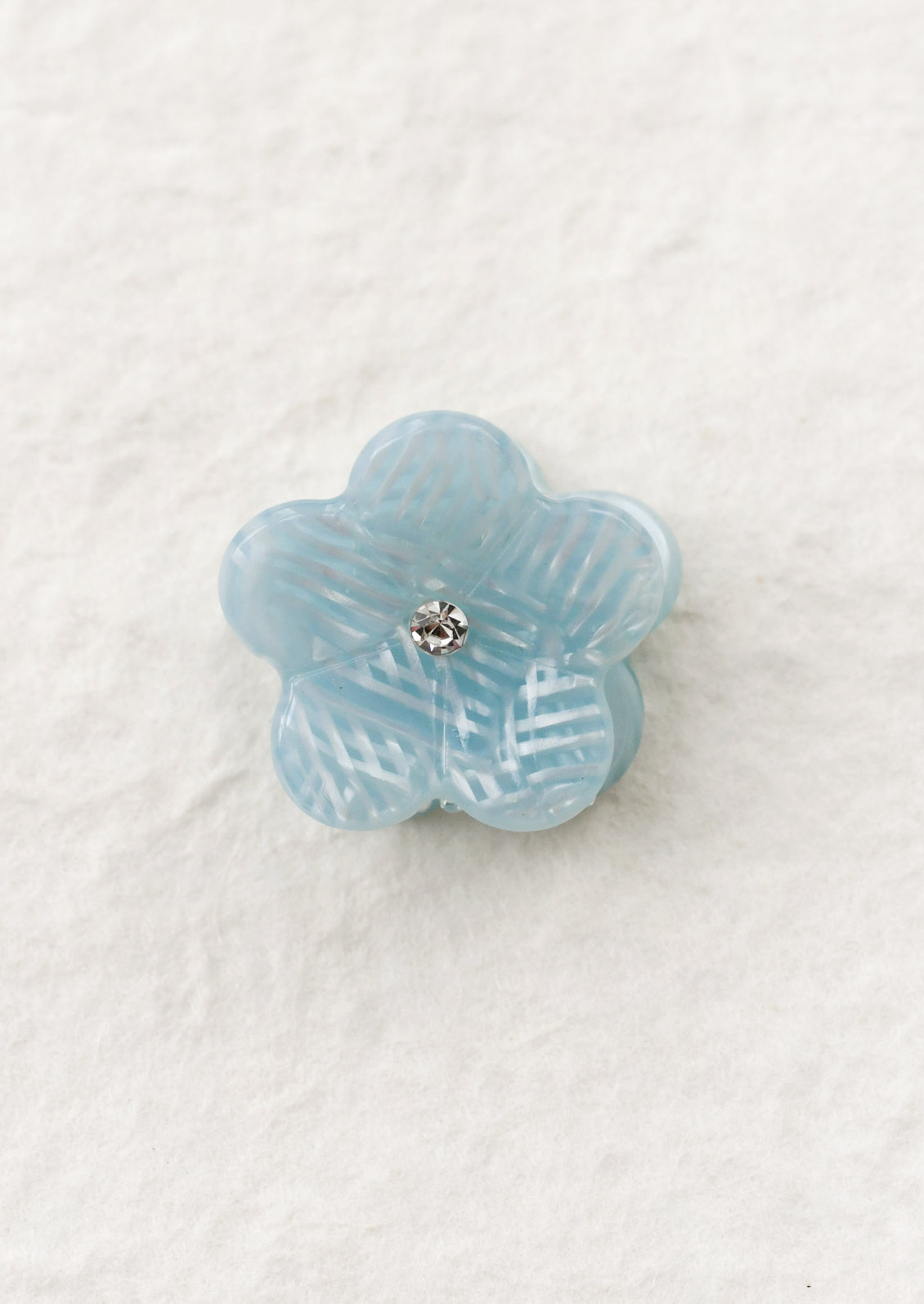 Blue flower-shaped mini hair claw on a textured white background
