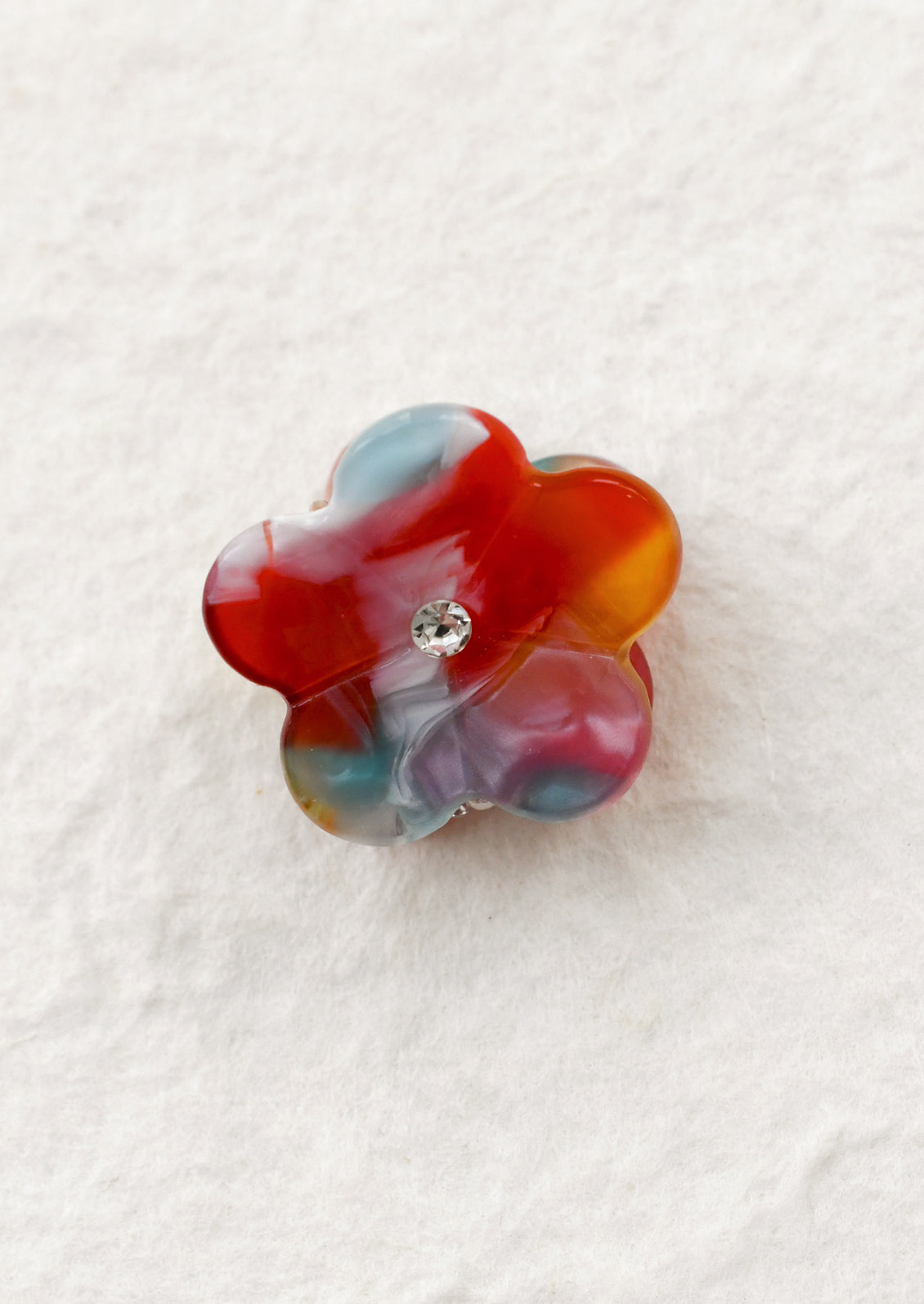 Multicolor flower-shaped hair claw with a central gemstone on a white background