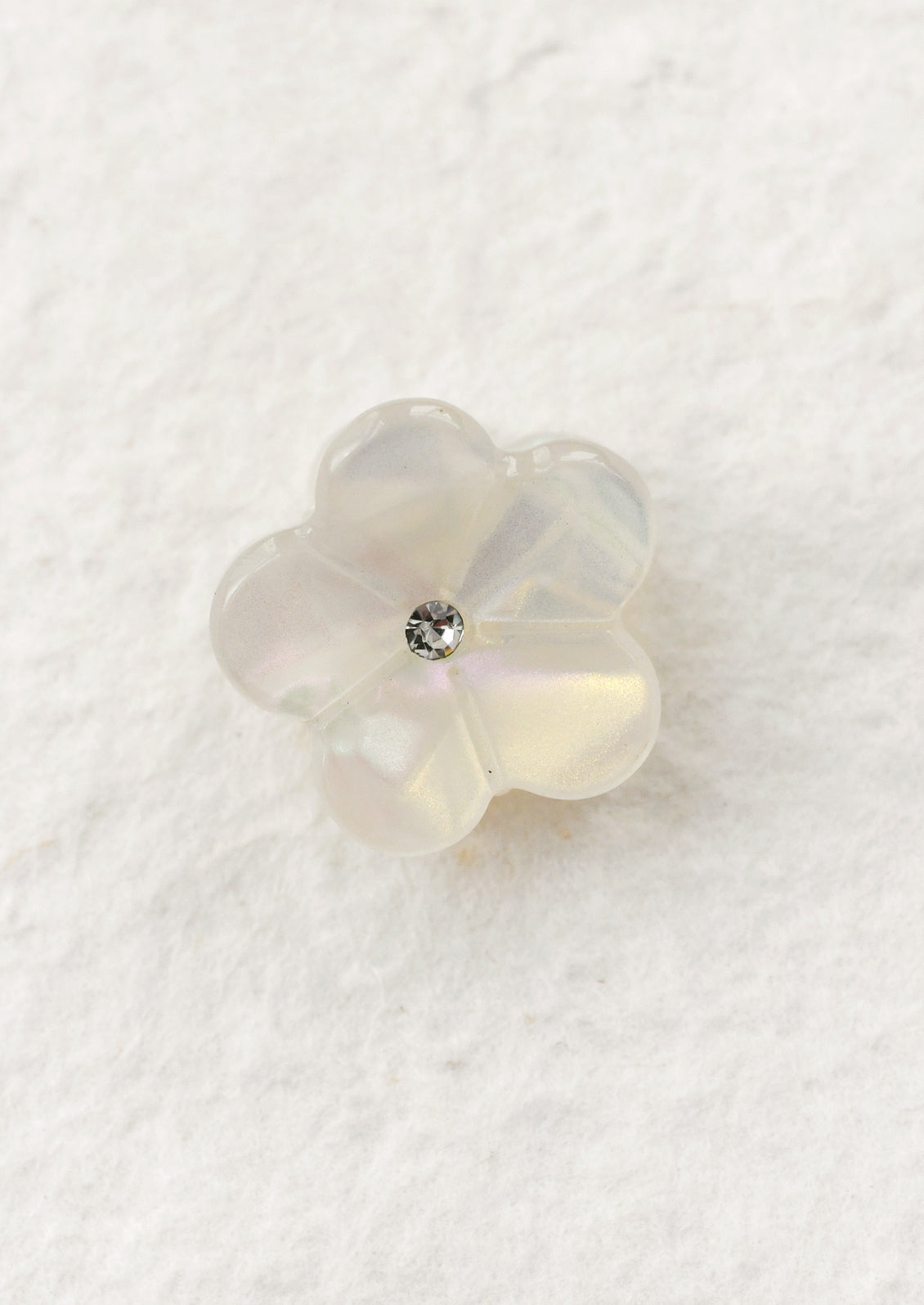 Pearl white flower-shaped mini hair claw on a textured white background