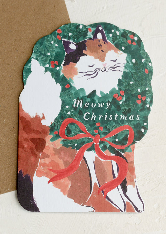 A diecut card depicting a cat wearing a wreath around its neck, text reads "Meowy Christmas".