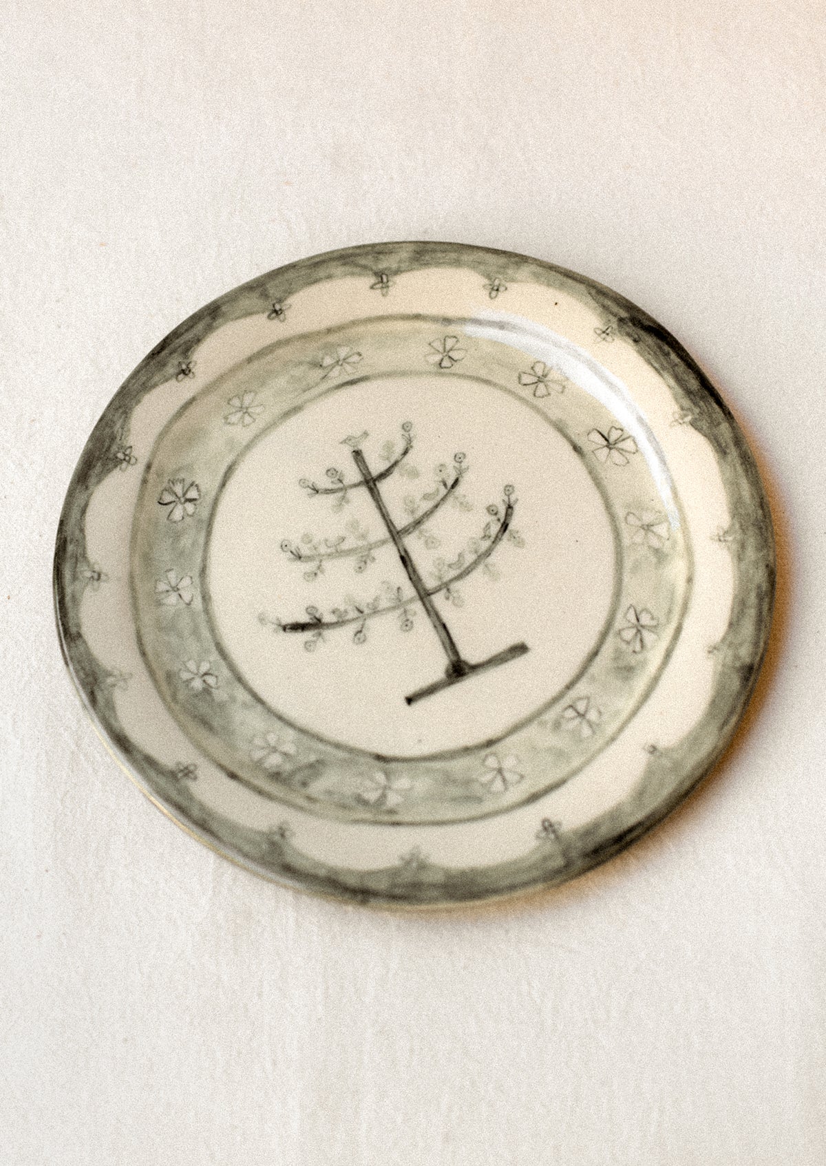 A cream ceramic plate with illustrated tree and flowers in dark grey.