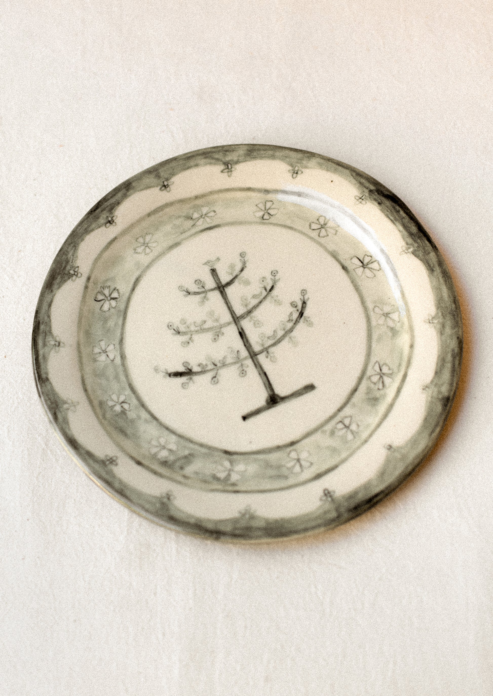 A cream ceramic plate with illustrated tree and flowers in dark grey.