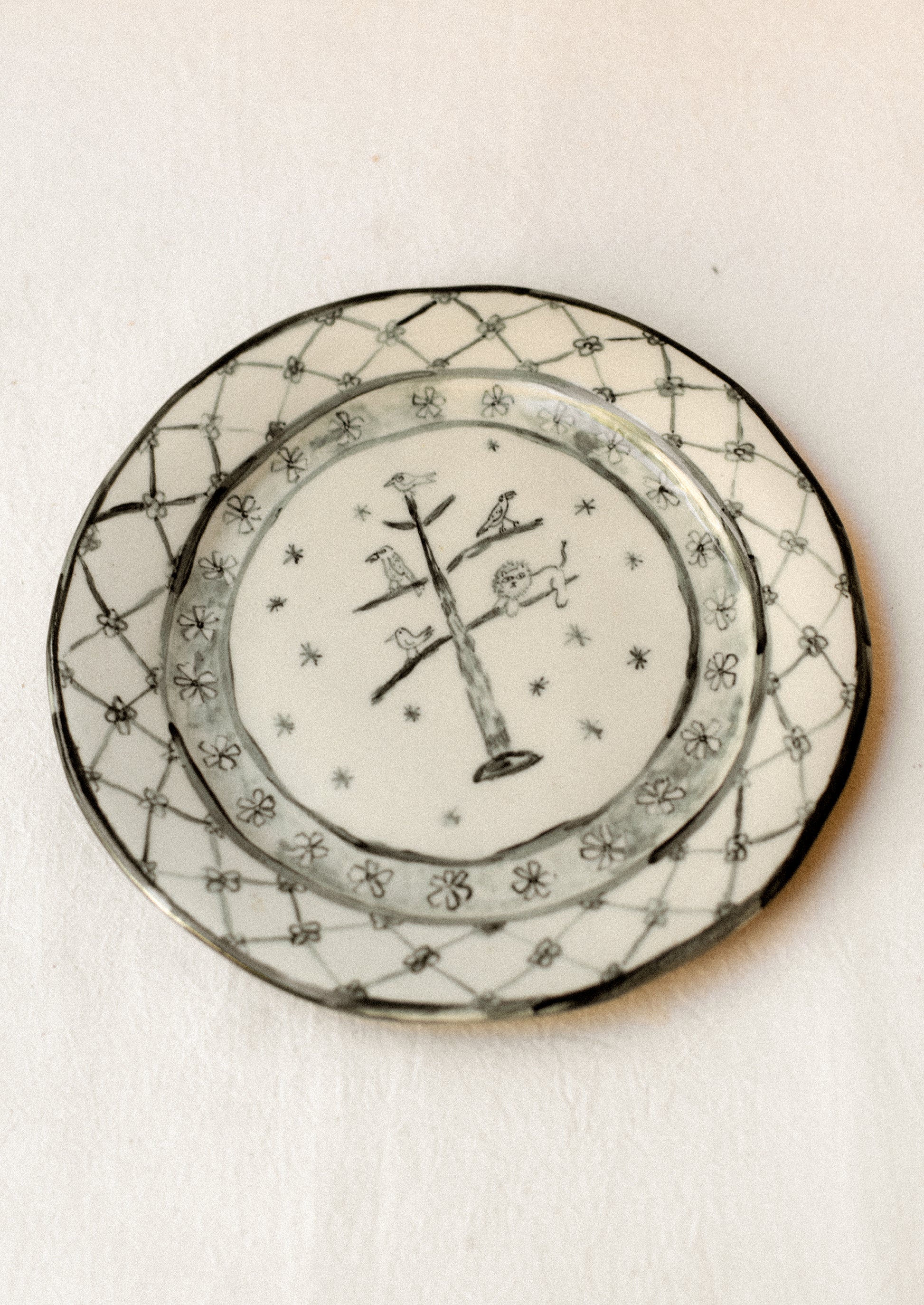 A cream ceramic plate with drawing of animals in tree and floral border in dark grey.