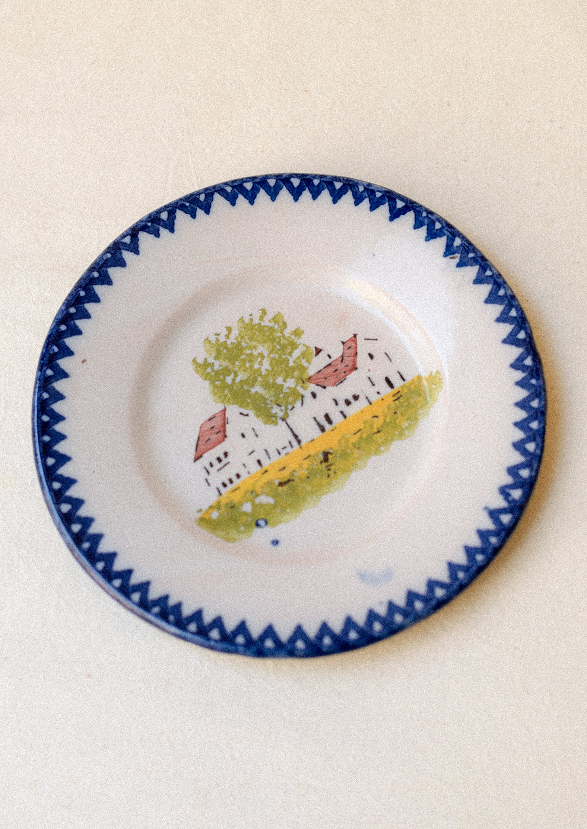 A plate with hand painted house motif and blue patterned rim.