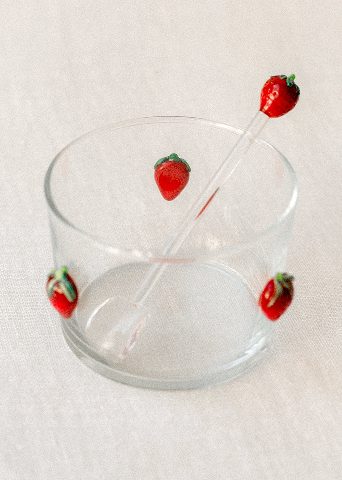 A clear glass spoon stirrer with red lampwork glass strawberry at end.