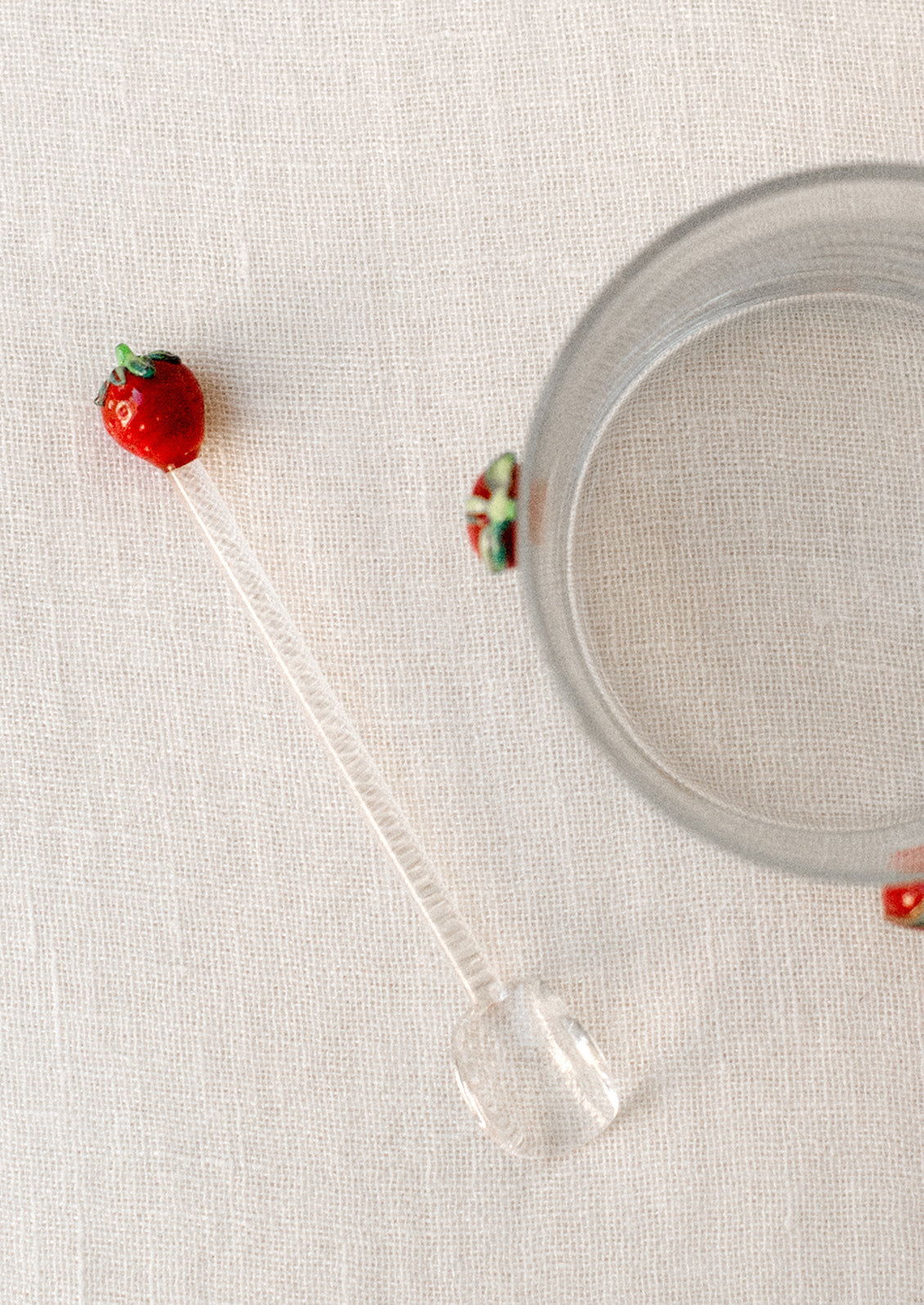 A clear glass spoon stirrer with red lampwork glass strawberry at end.