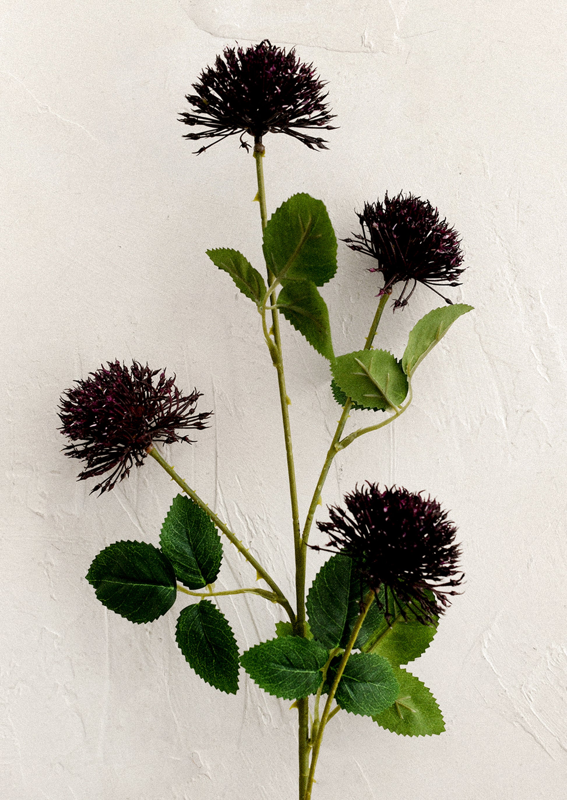 A faux flower spray in the likeness of a globe thistle plant, in dark purple.