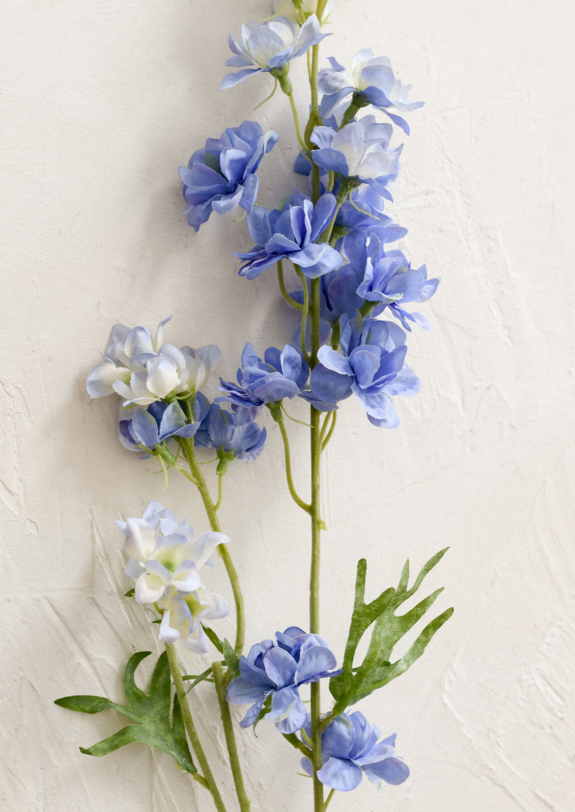 A faux flower stem depicting a periwinkle larkspur flower spray.