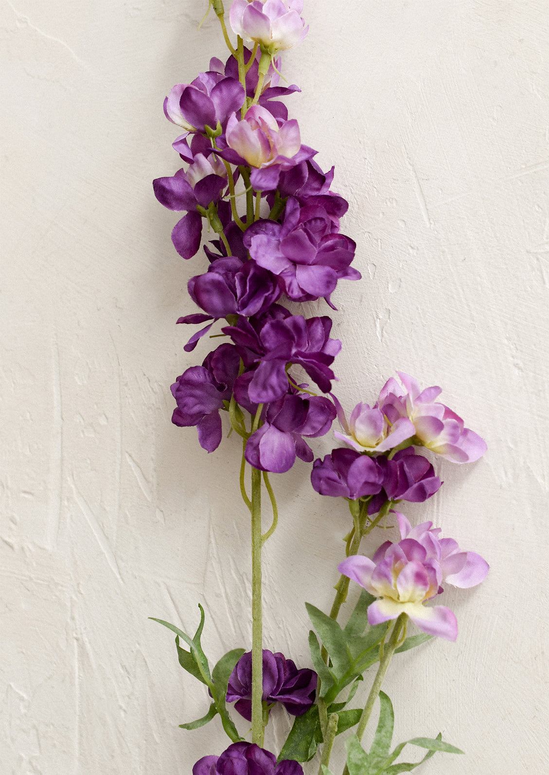 A faux flower stem depicting a purple larkspur flower spray.
