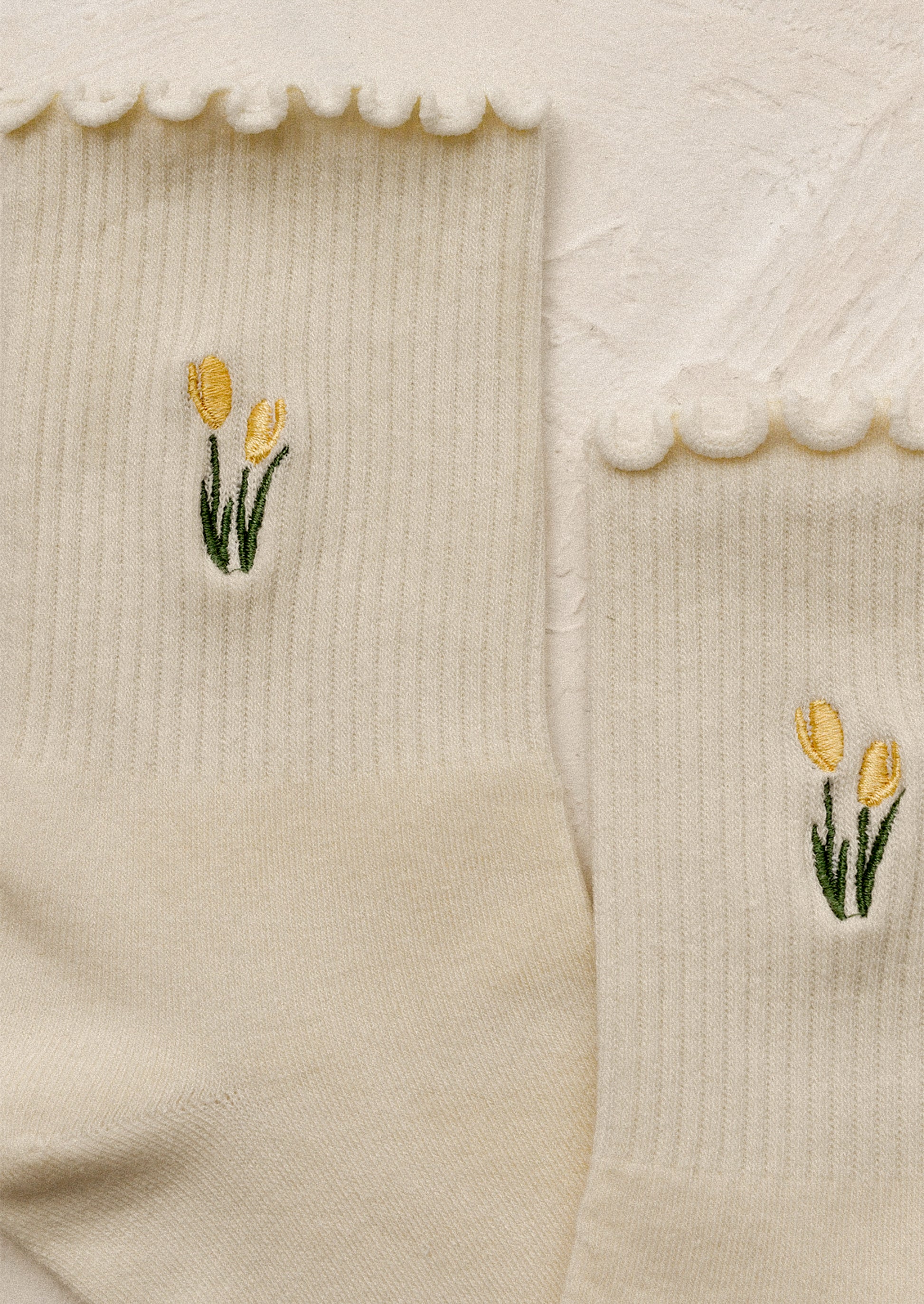 A pair of cream socks with embroidered tulip motif in butter yellow.