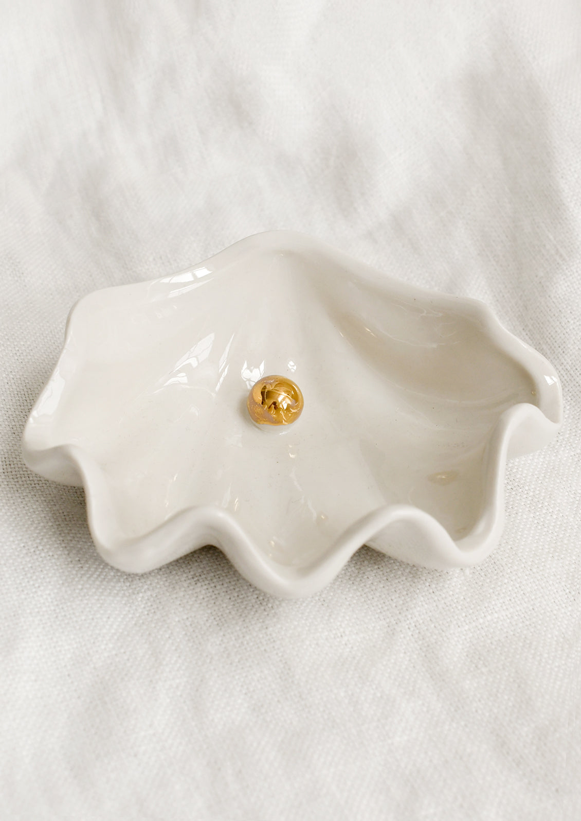 An oyster shaped ceramic bowl in white with gold pearl detail at center.