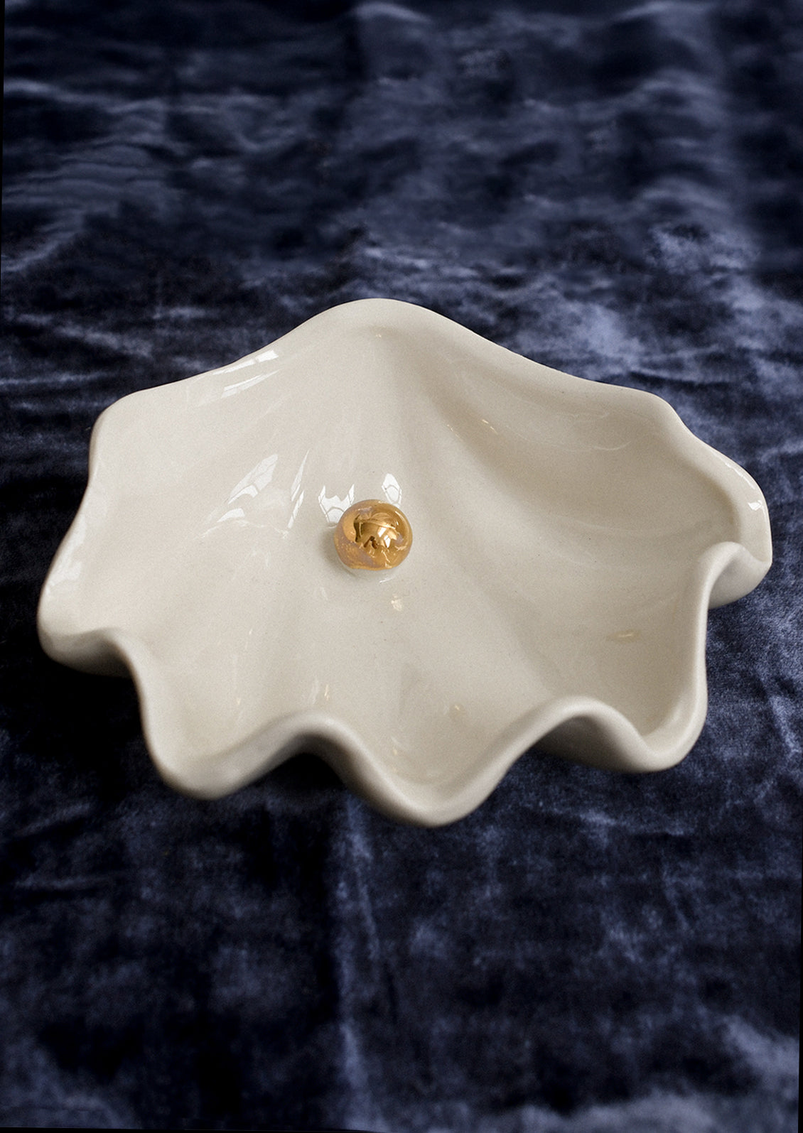 An oyster shaped ceramic bowl in white with gold pearl detail at center.