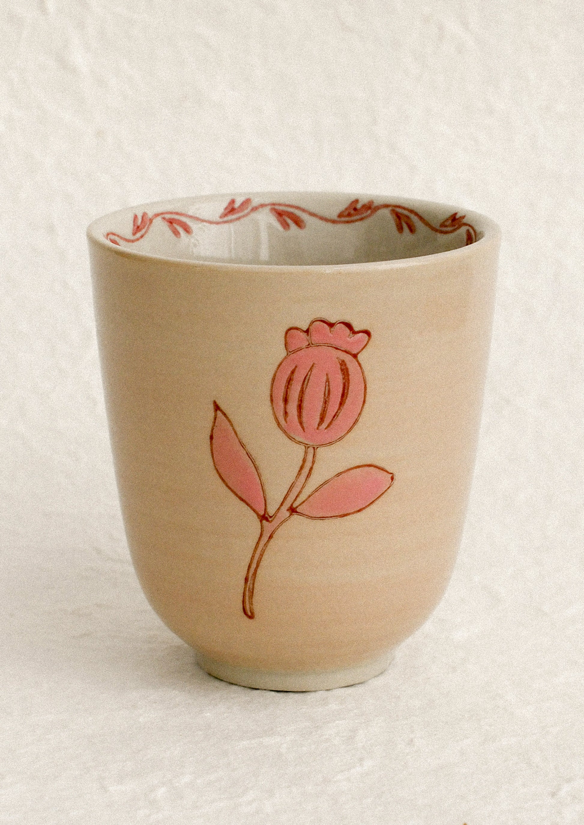 A beige ceramic cup with pink floral print and trim around inside rim.