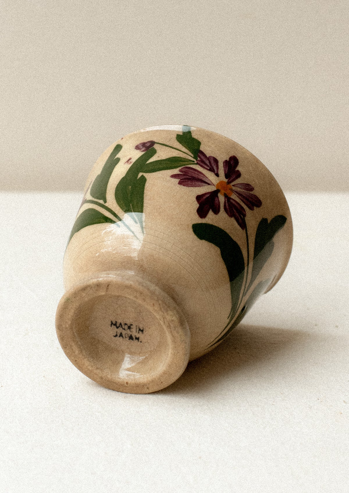 A tan ceramic antique tea cup with purple floral pattern.