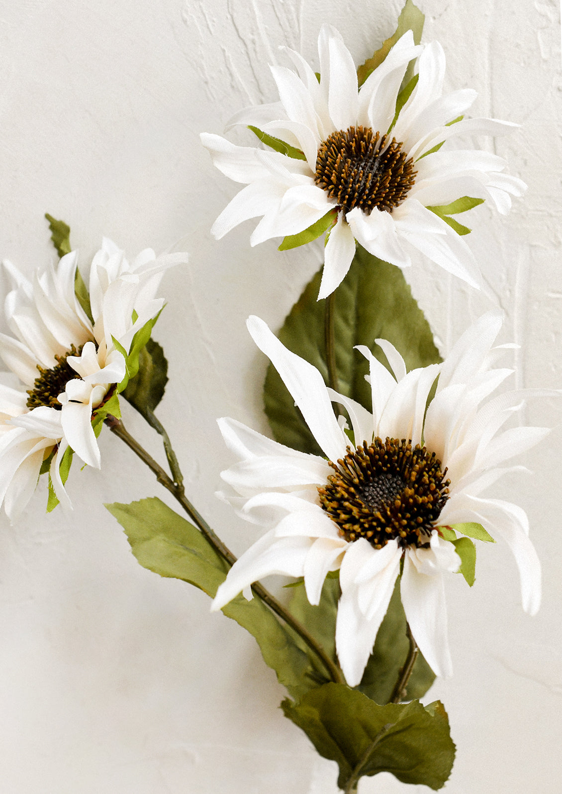 A faux floral spray depicting cream colored sunflowers.