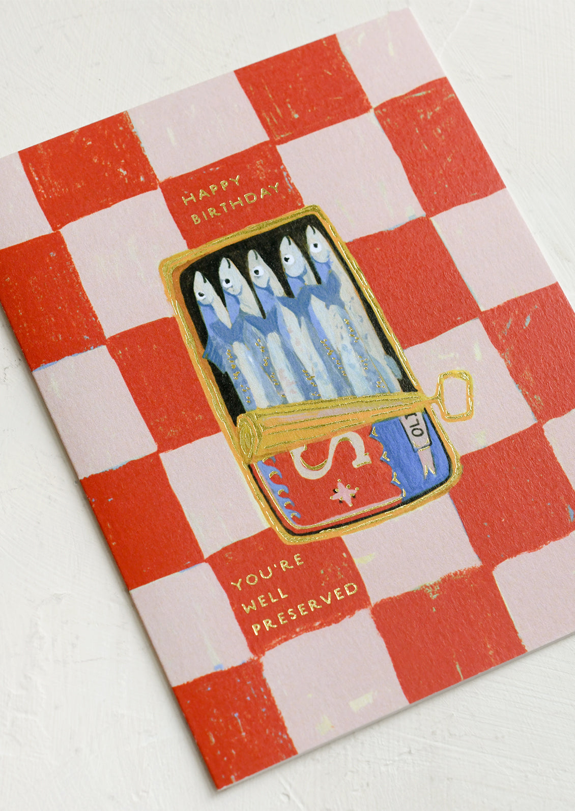 A red and pink checkered card with illustration of tin of sardines, texts reads "Happy Birthday, you're well preserved".