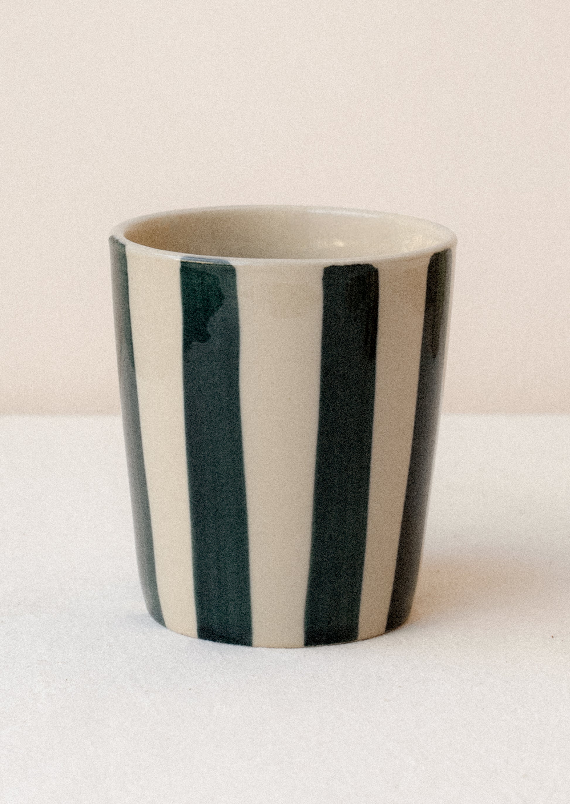 A striped ceramic cup in bisque with navy stripes.