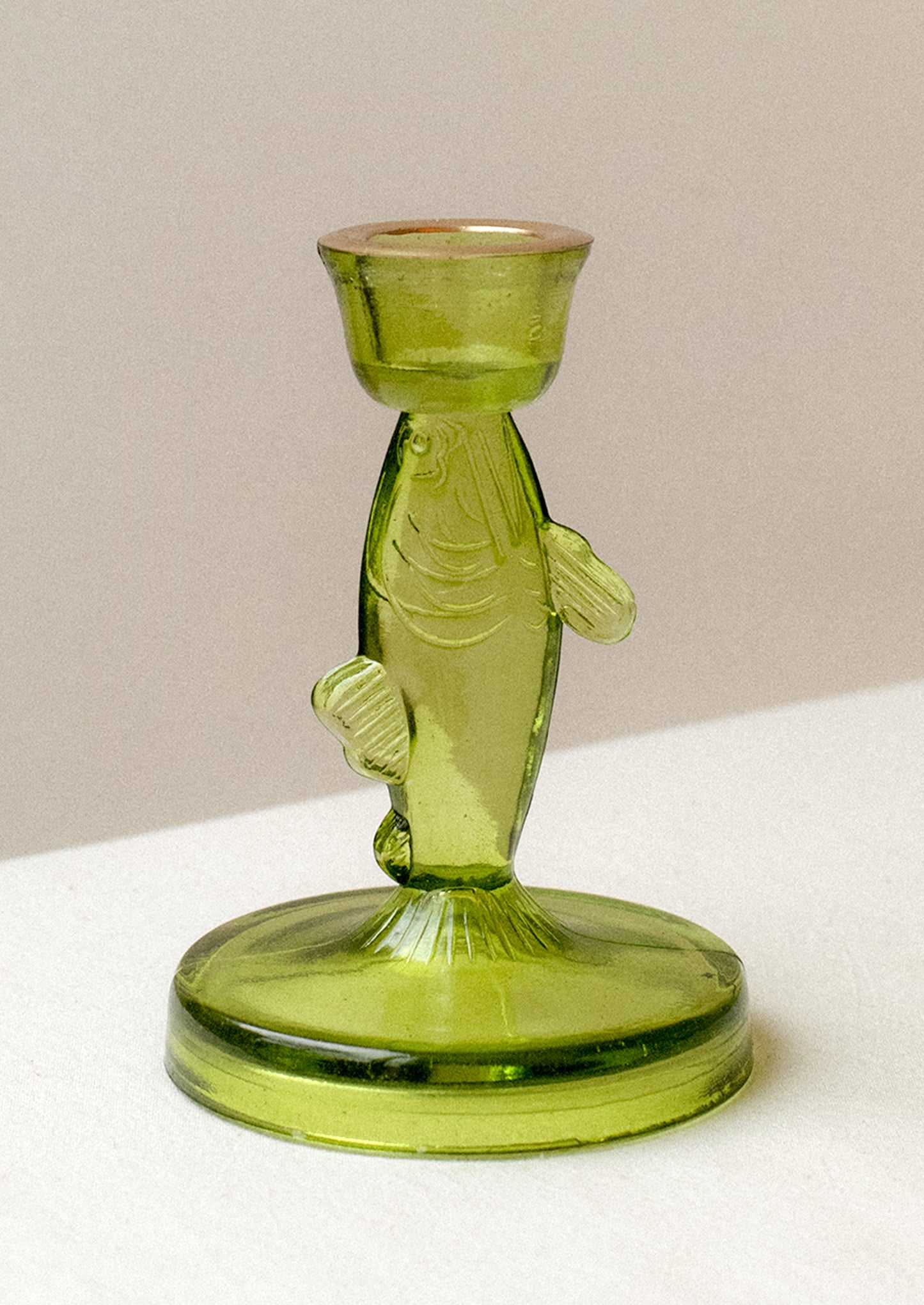 A green tinted translucent glass candle holder in the shape of a fish.