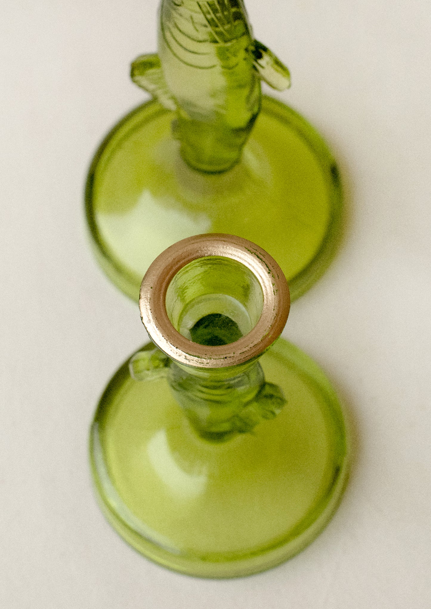 A green tinted translucent glass candle holder in the shape of a fish, with gold detailing along rim.