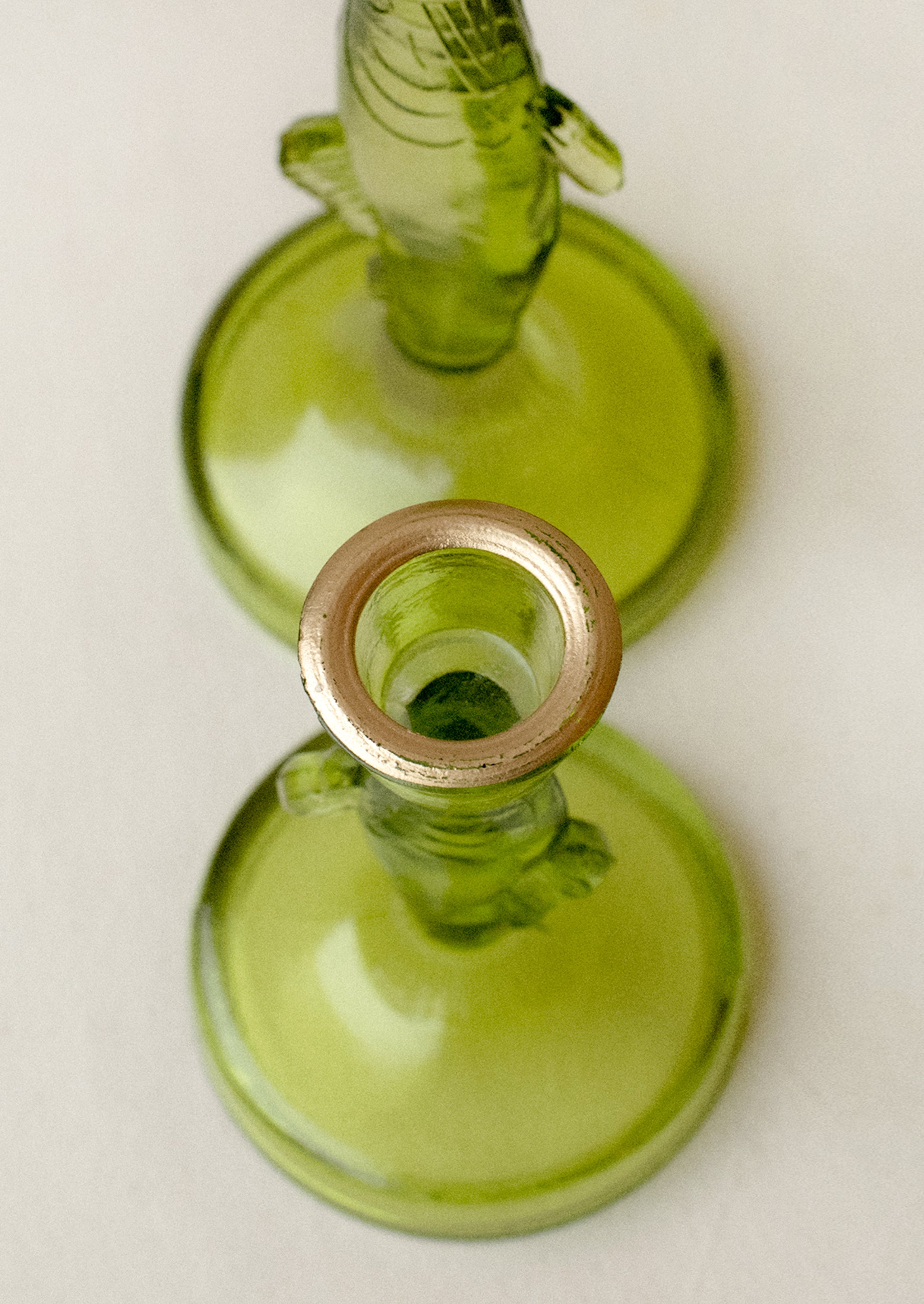 A green tinted translucent glass candle holder in the shape of a fish, with gold detailing along rim.