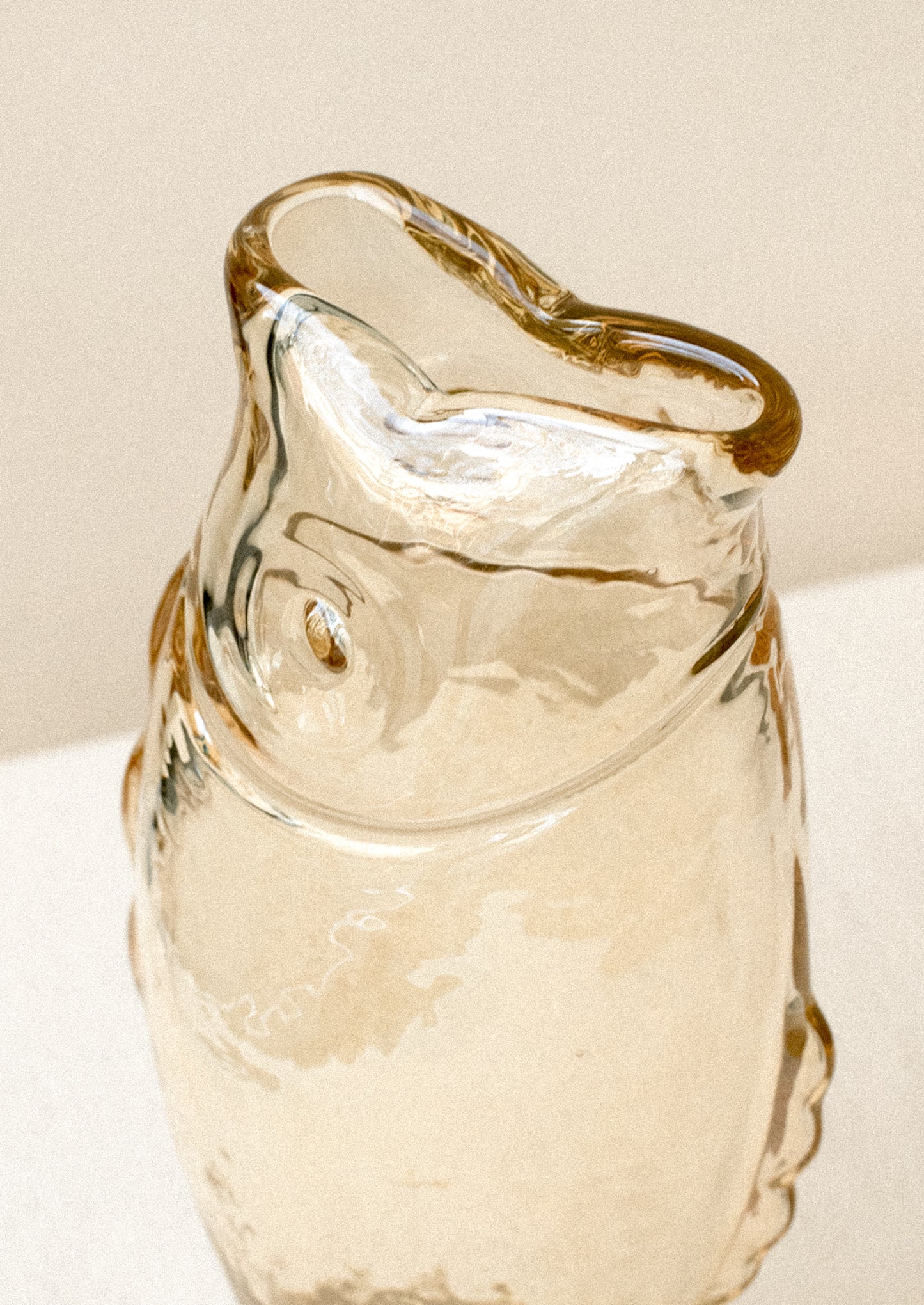 A transparent glass vase in the shape of a fish, in pale brown color with subtle iridescence.