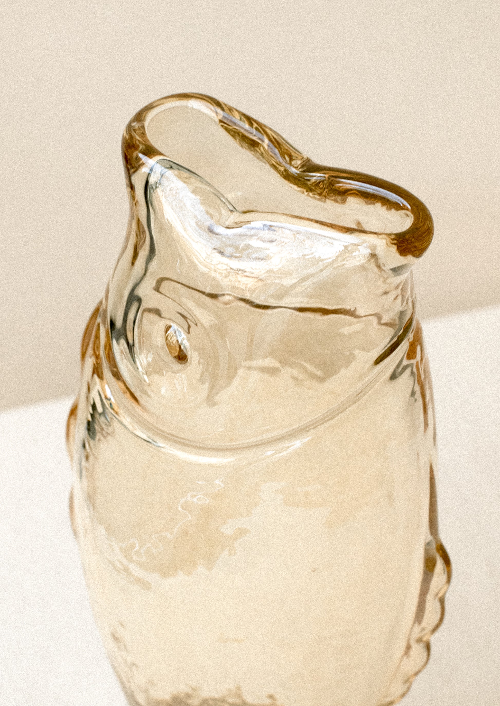 A transparent glass vase in the shape of a fish, in pale brown color with subtle iridescence.