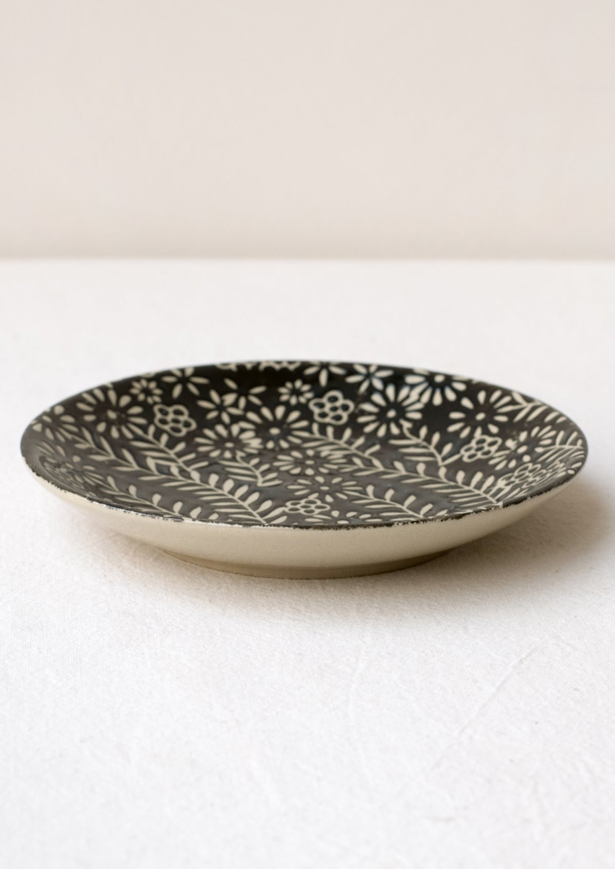 A small side plate with wax relief floral pattern in black and white.