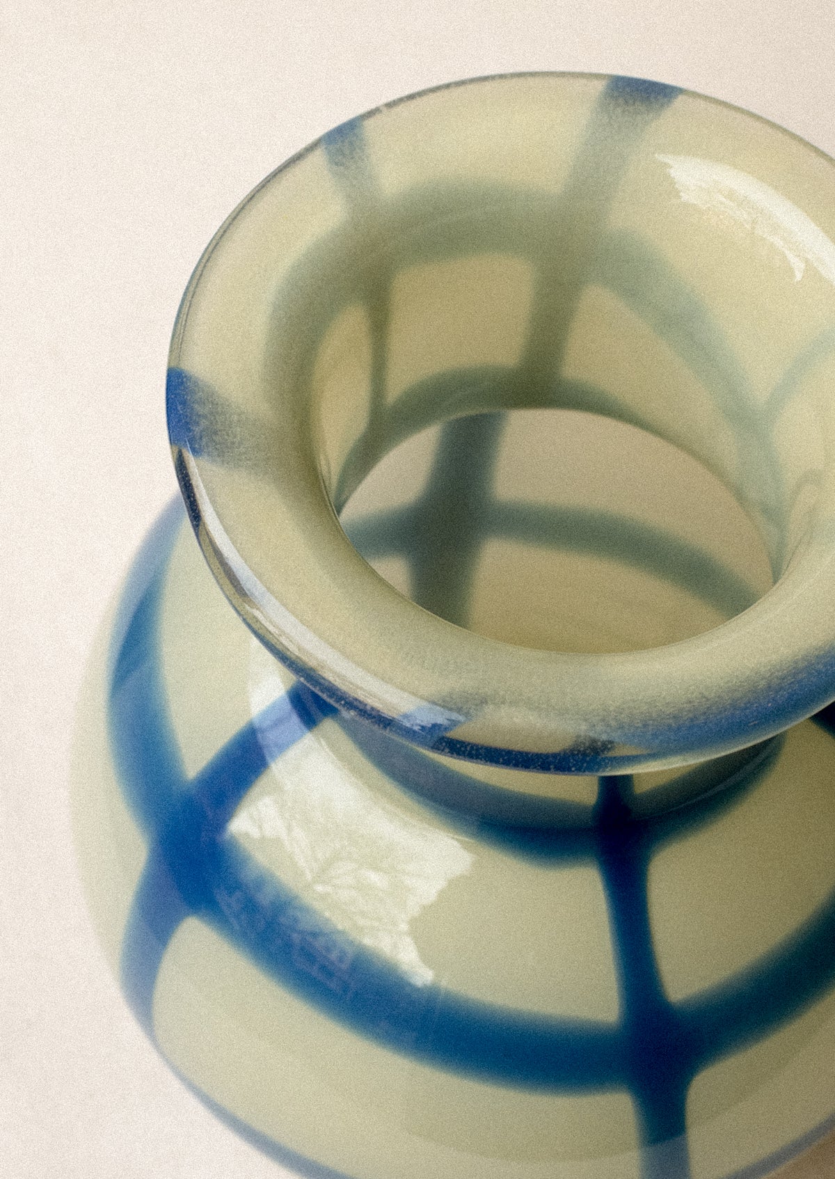 A glass vase with round shape, in yellow with painted blue gingham pattern.