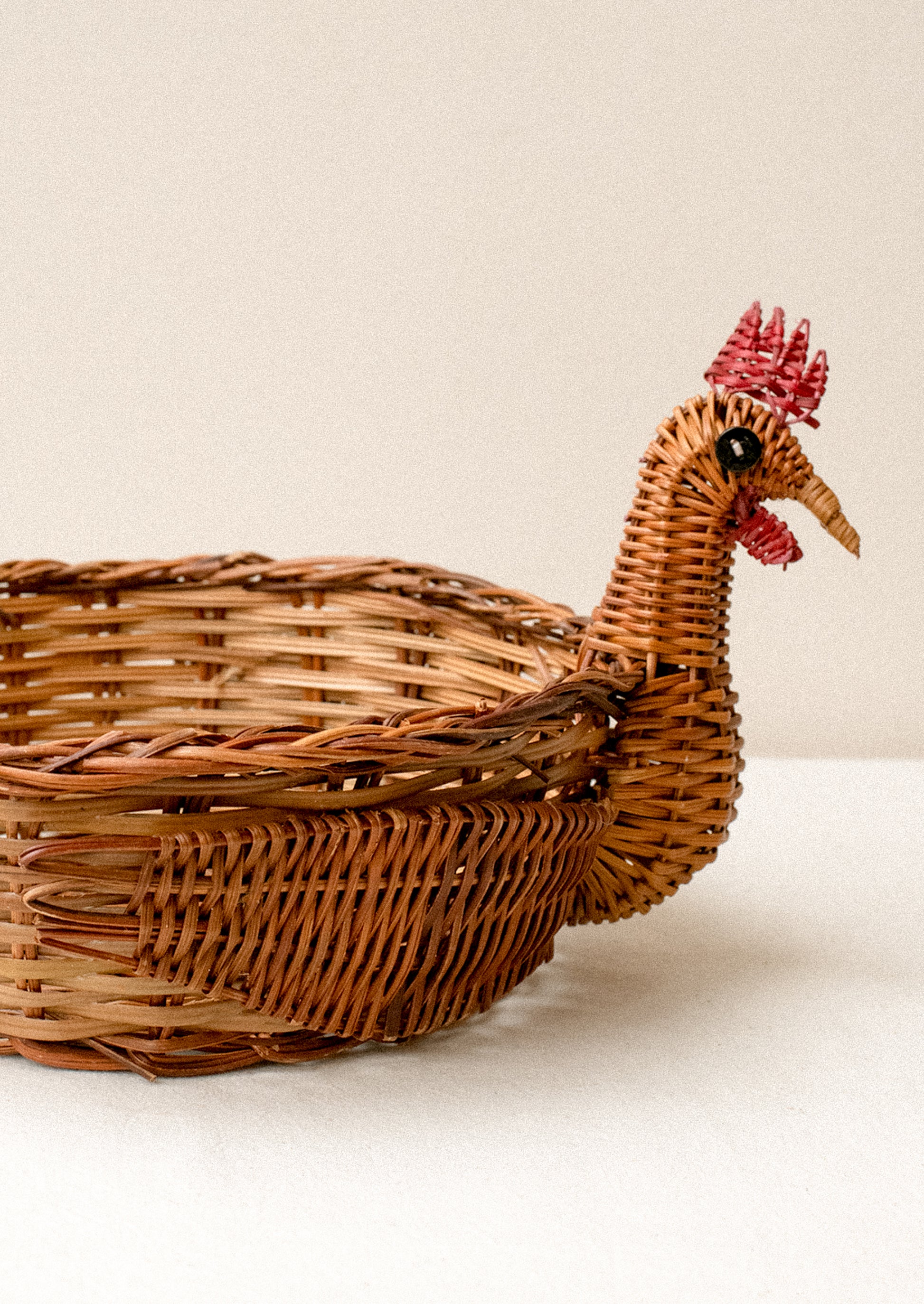 A woven basket with three dimensional chicken head detailing on side.