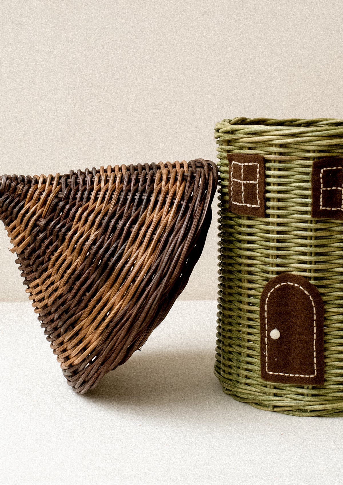 A round rattan basket in the shape of a house, with window and door detailing, lid is the roof.