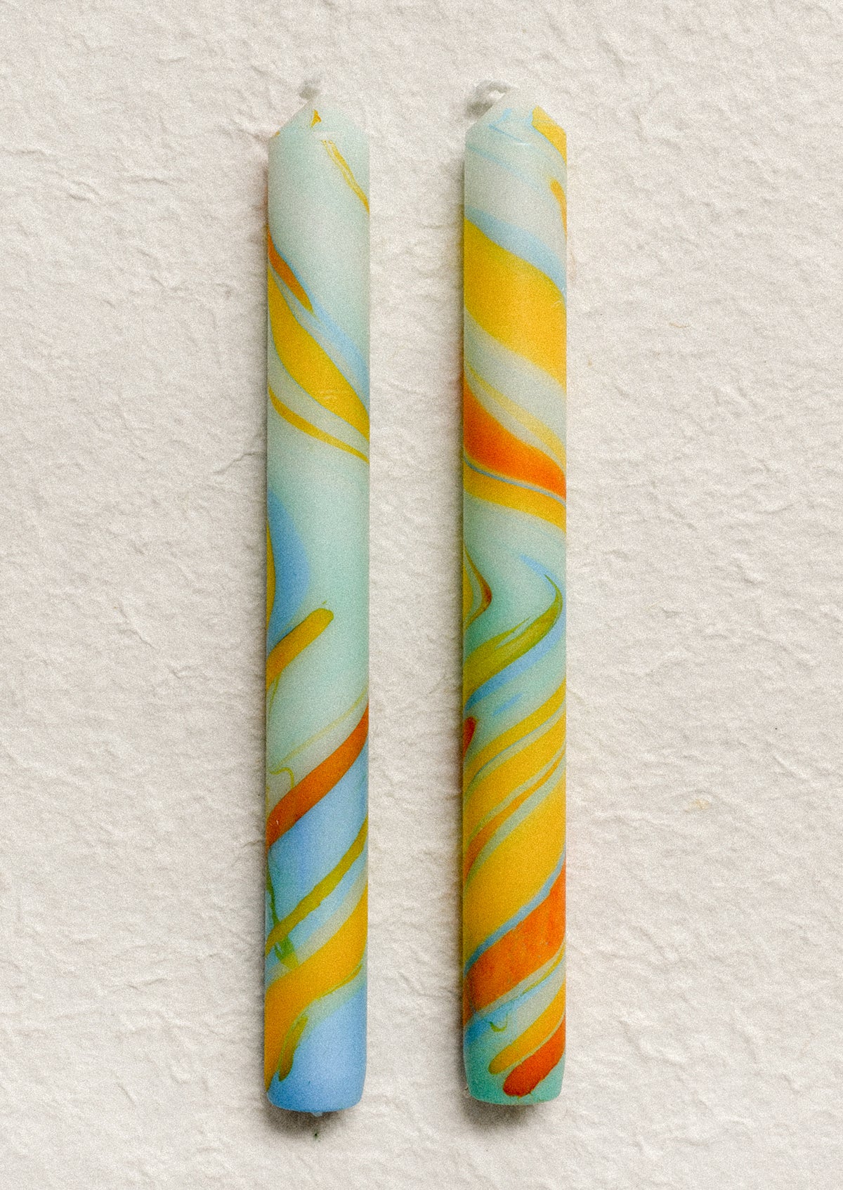 A marbled taper candle in blue, orange and yellow swirl pattern.